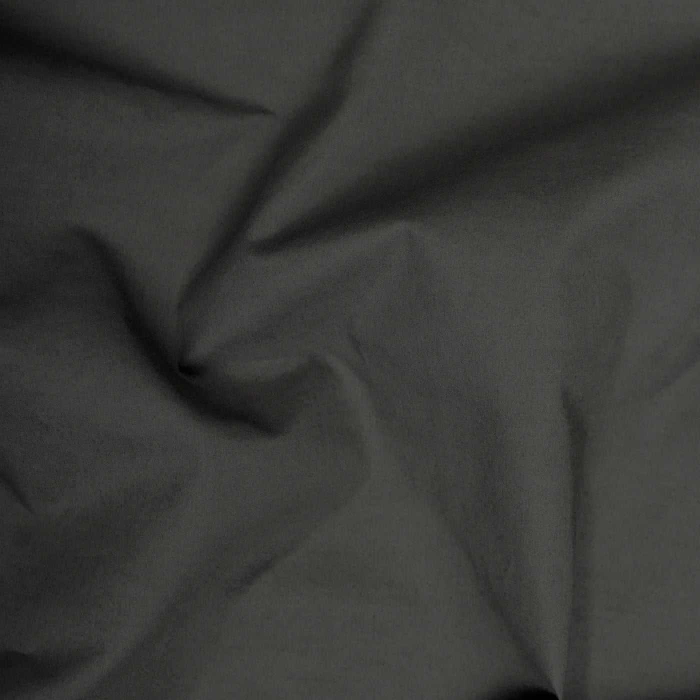 A close-up of the Riviera Cotton Wash Towel in Coal shows dark gray, garment-dyed cotton with natural folds and creases, highlighting the towel’s soft texture and subtle shadows.