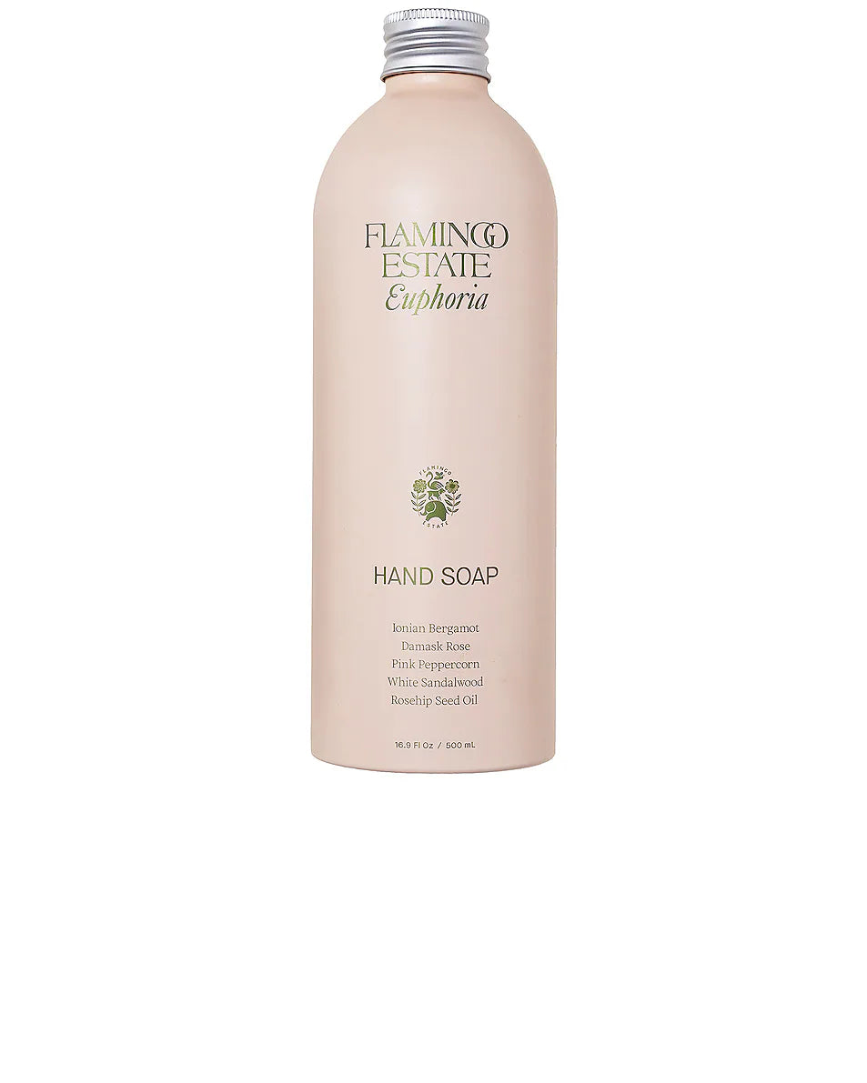 A light pink bottle of Flamingo Estate - Jasmine Damask Rose Hand Soap with a silver cap, gold embossed logo, small green tree graphic, and a label featuring key ingredients like jasmine and damask rose.