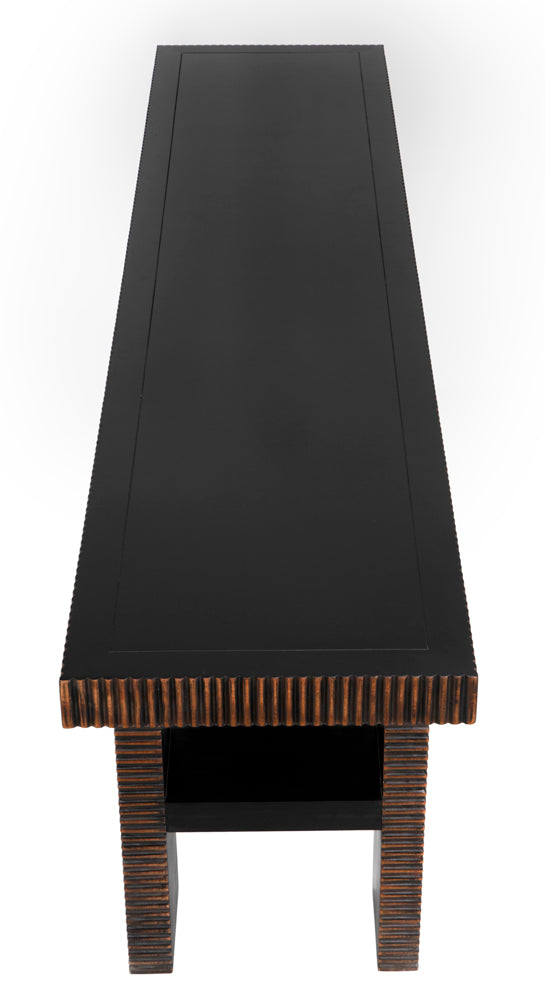 The Nabu Console in hand rubbed black with light brown trim is a long, rectangular table featuring textured grooved edges and thick patterned legs connected by a mahogany shelf. Photo shows the piece from above one end.