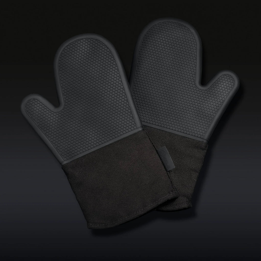 The Hexclad Mitt Set of 2, featuring black silicone oven mitts with textured surfaces and fabric cuffs, is shown overlapping on a dark gradient background.
