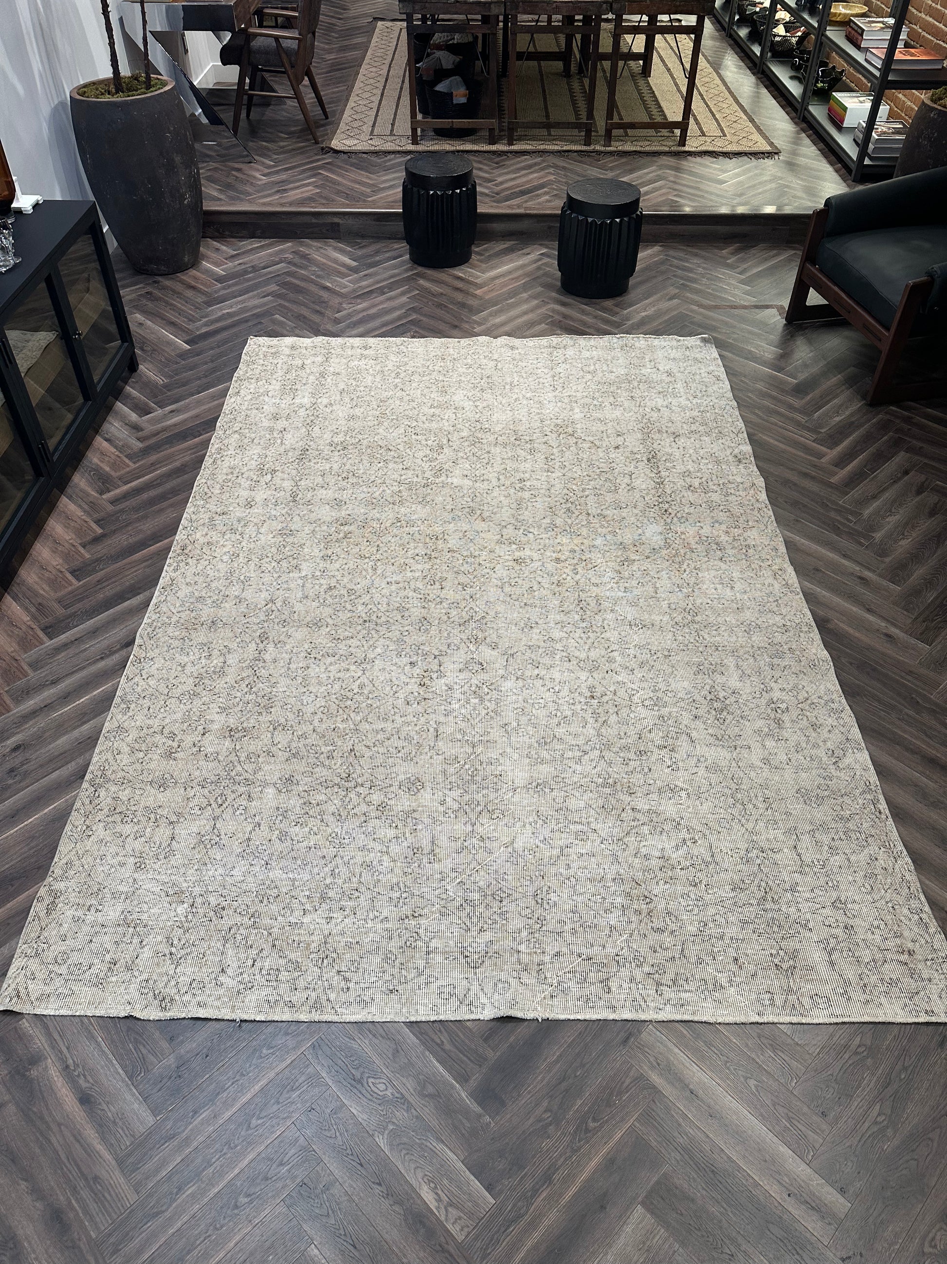 A Reversible Vintage Rug with a subtle pattern is laid out on a dark herringbone wood floor in a modern room featuring black furniture and decor.