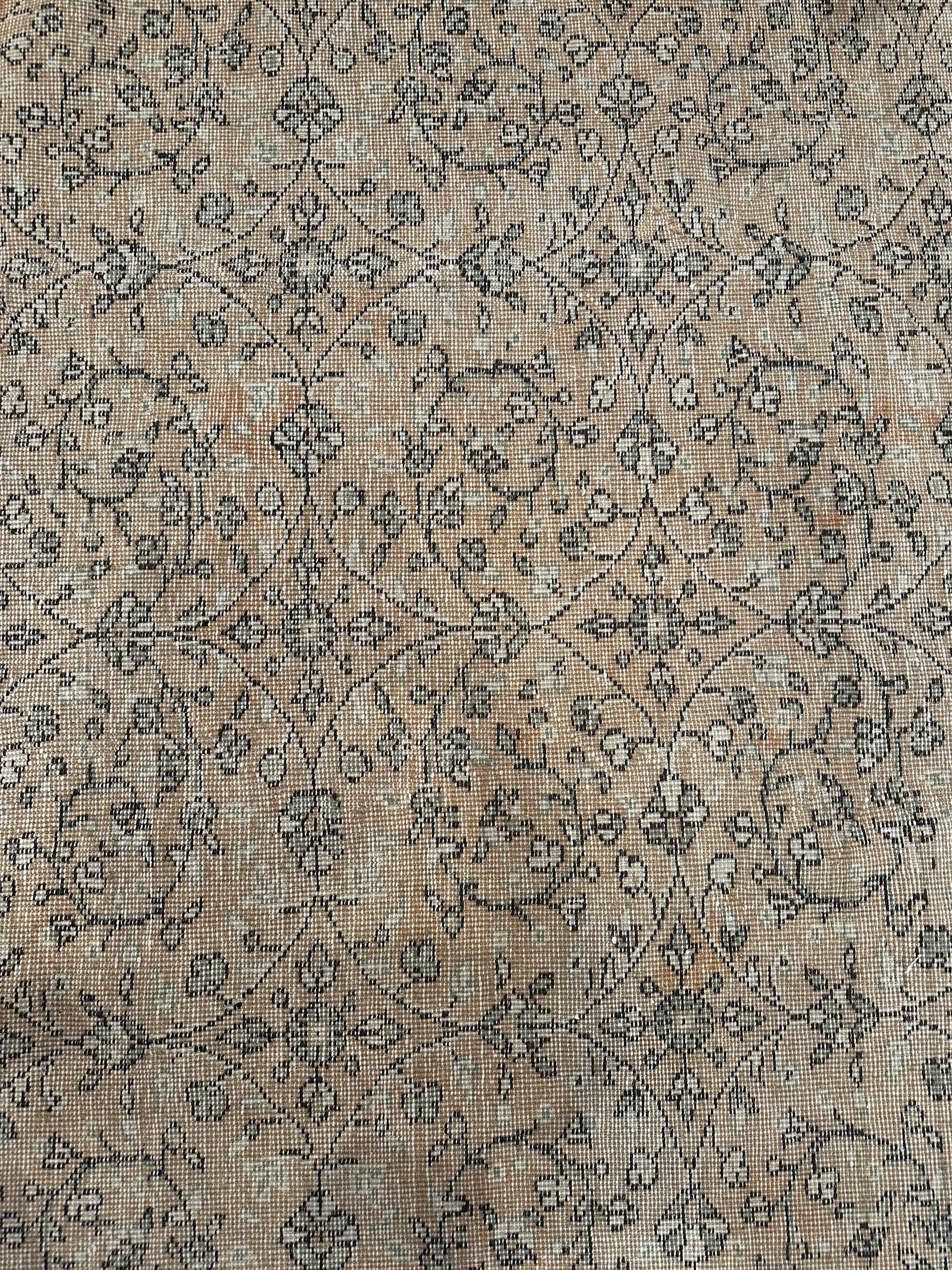 A close-up of the Reversible Vintage Rug reveals a faded beige background with intricate, repeating floral and vine motifs in muted brown and gray, showcasing its fabric’s texture and charming vintage wear.
