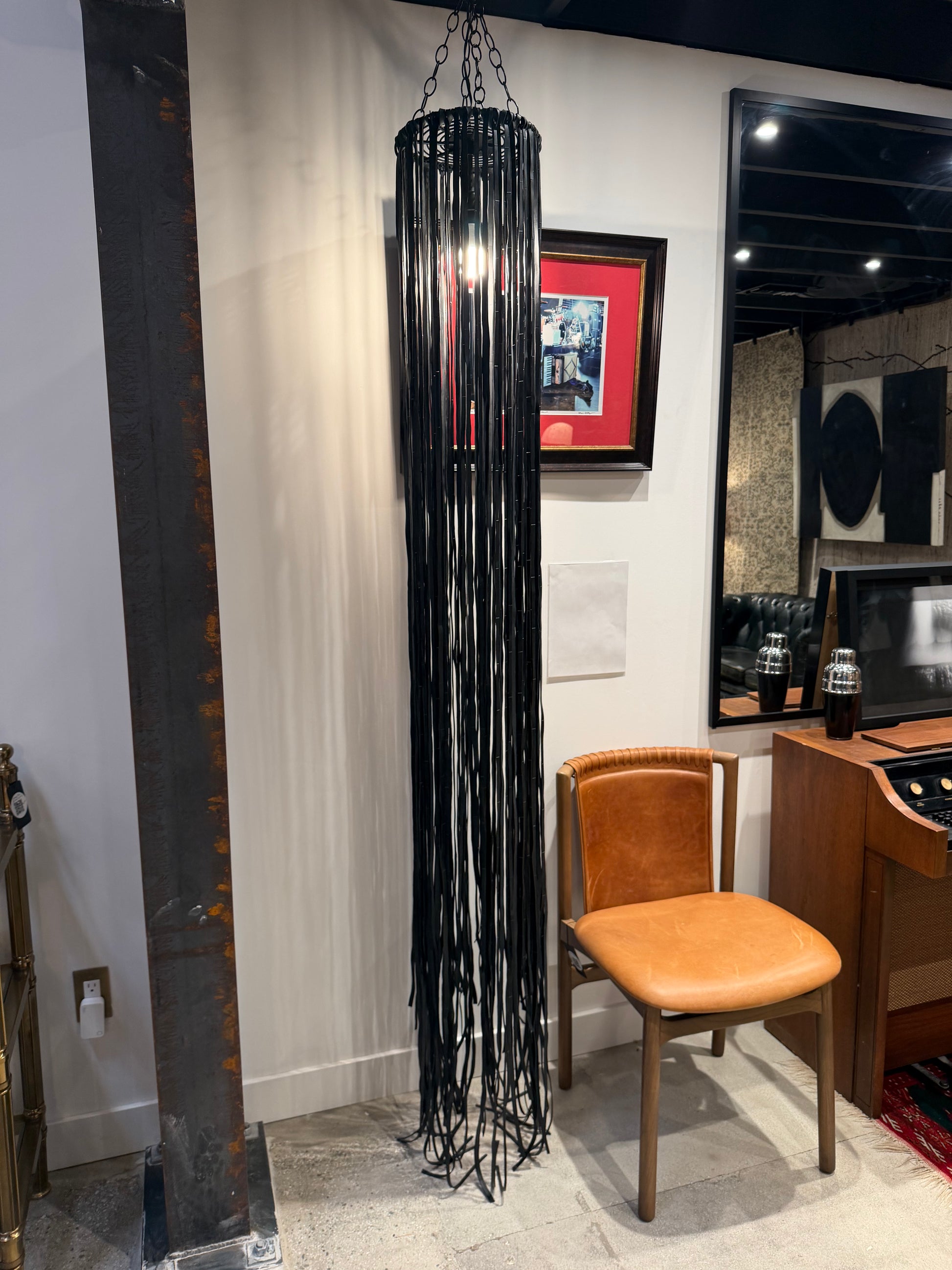 A tall, cylindrical Black Vegan Leather Fringe Pendant light fixture featuring a metal frame covered in long, black rubber fringe.