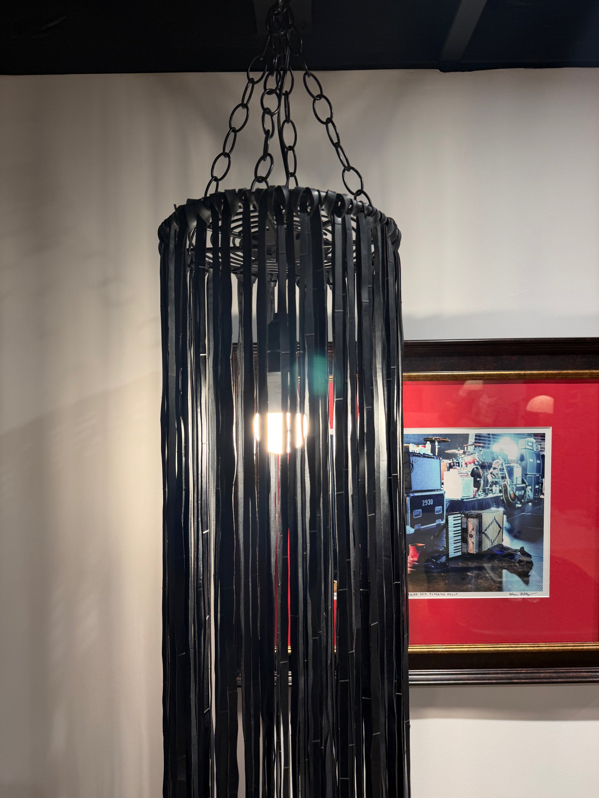 A Black Vegan Leather Fringe Pendant featuring a cylindrical metal frame draped with long, vertical black rubber fringe strips.
