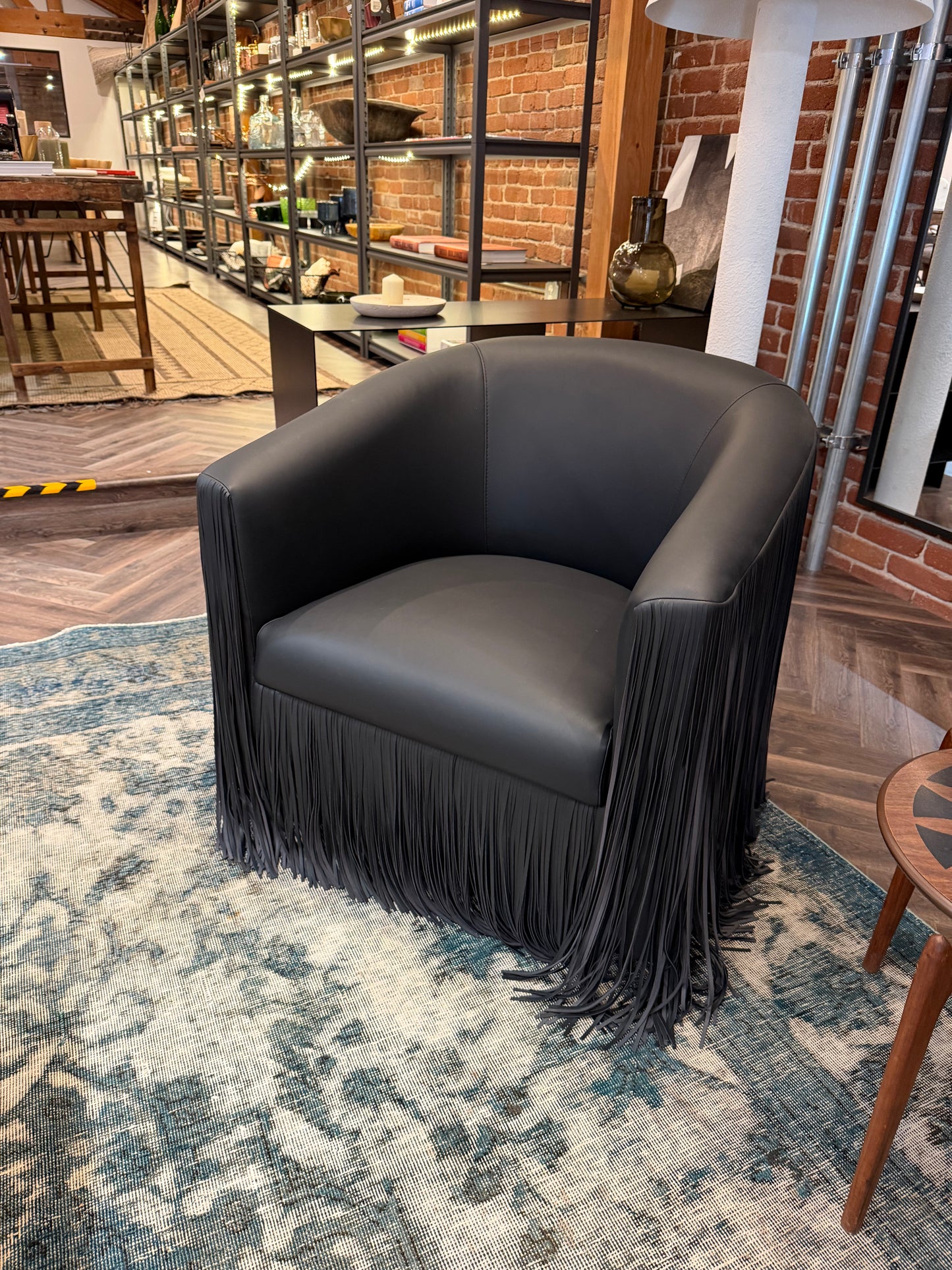 Black Leather Fringe Lounge Chair with a curved back and long fringe trim along the bottom, shown with specified furniture size and sofa dimensions.