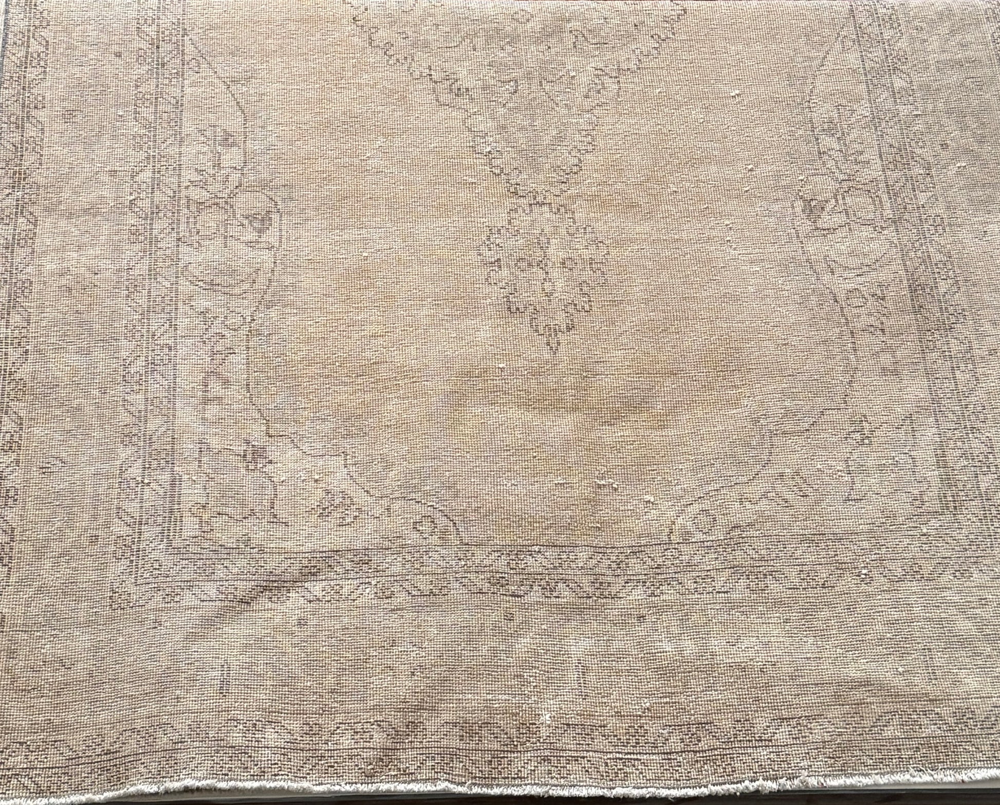 Introducing the 7' x 11' Dark Beige Vintage Rug, featuring subtly faded floral and geometric patterns along the border and center. The muted tones and frayed edges create an authentically worn look, adding timeless, rustic charm to any space.