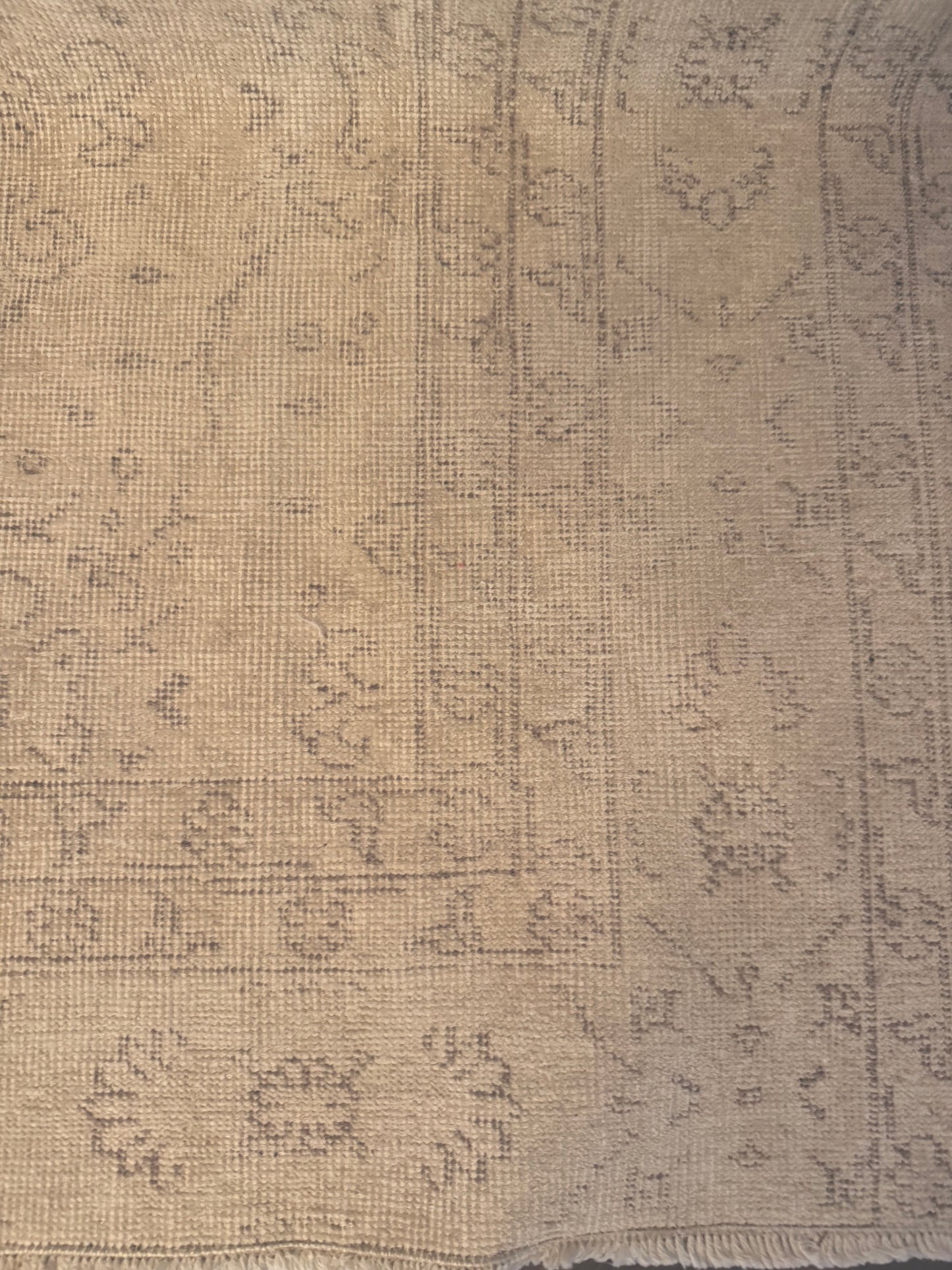 A 6'x9' Cream Area Rug featuring a vintage-inspired faded floral and geometric pattern in beige tones. The rug's worn texture and fringed bottom edge lend a charming, timeless appeal to any space.