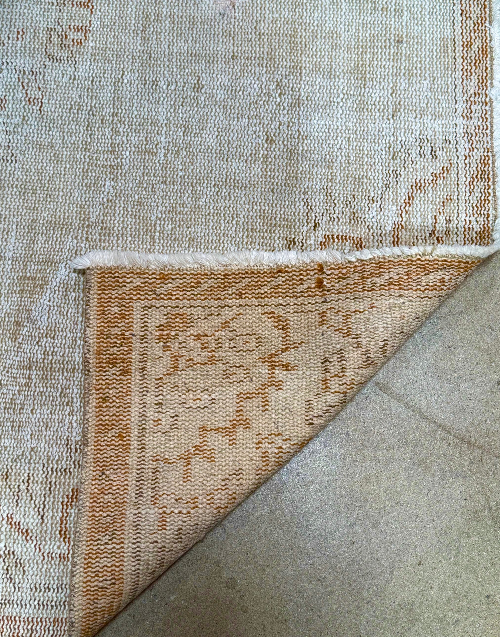 The Vintage Cream/Sienna Reversible Rug, measuring 8'10" x 4'8", is shown with one corner flipped to display its patterned underside featuring tan and cream designs. It rests on a smooth, light-colored floor.