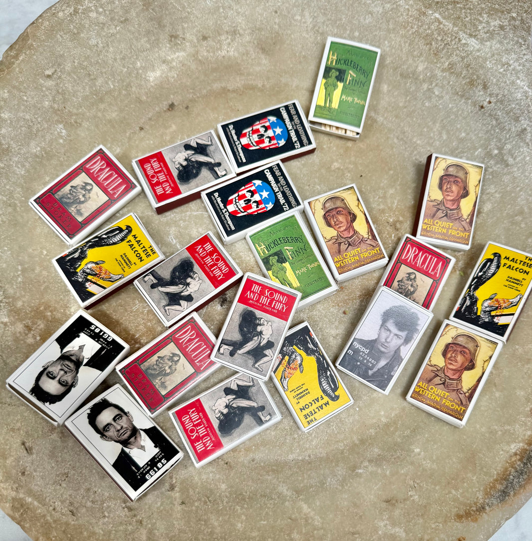 A set of Vintage Matchbook collectibles, featuring charming floral designs, classic portraits, and various iconic book cover styles, artfully scattered on a textured beige stone surface.