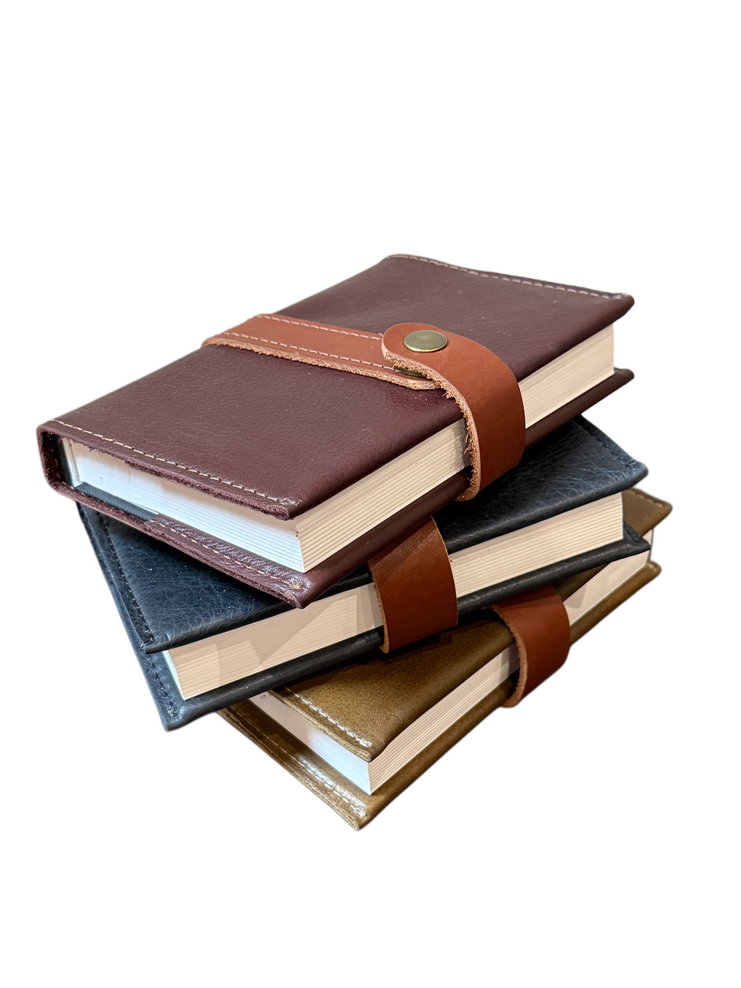 Three closed Writer's Journals, featuring handcrafted leather covers in brown, black, and gold, are stacked atop one another. Each journal is fastened with a brown strap and button, making them the perfect custom branded keepsake. The background is white.