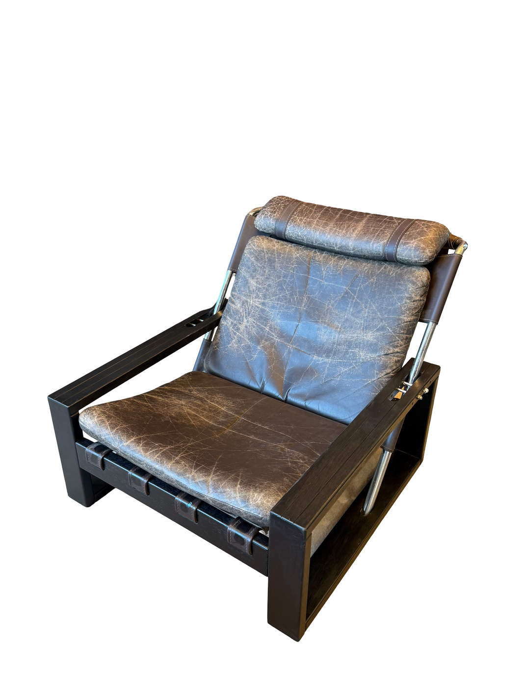 The 70s Brutalist Lounge Chair features distressed brown leather upholstered cushions, a black lacquered oak frame, and metal arm supports, displayed against a white background.