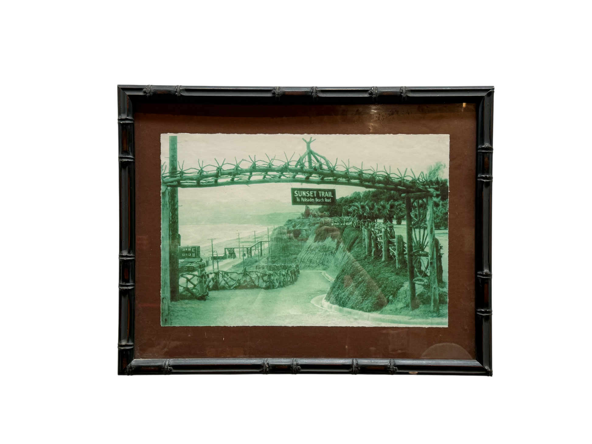 The Sunset Trailhead Framed Photograph showcases a vintage, green-tinted image of a gated entrance marked “Sunset Trail,” featuring a scenic path, palm trees, and rolling hills in the background. Measuring 22.5″ x 17.5″, this classic-sized piece is an eye-catching addition to any space.