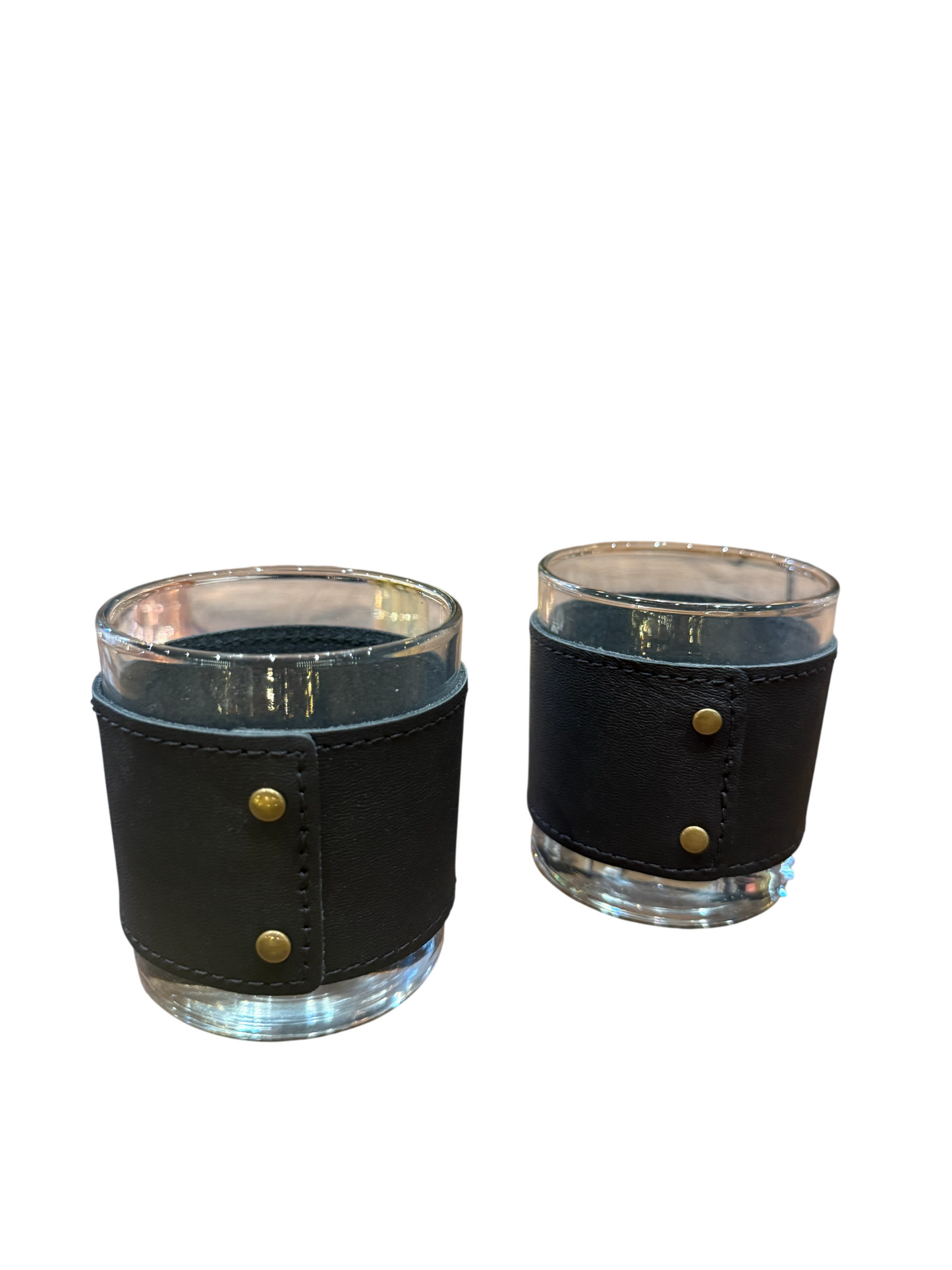 The Leather Wrapped Tumbler Set features two clear glass tumblers, each wrapped in a black leather sleeve and finished with brass stud accents, displayed on a white background.