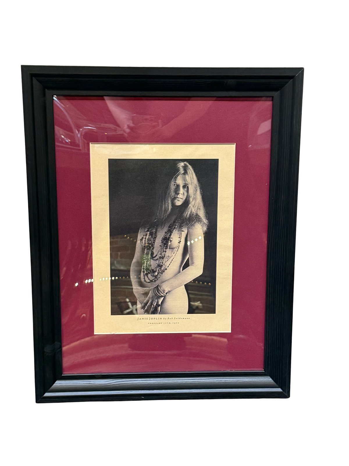 A framed 14.5 x 19 black-and-white Janis Joplin Beaded Cape by Bob Seidemann portrait of Janis Joplin wearing beaded necklaces, with text at the bottom including her name and a date.