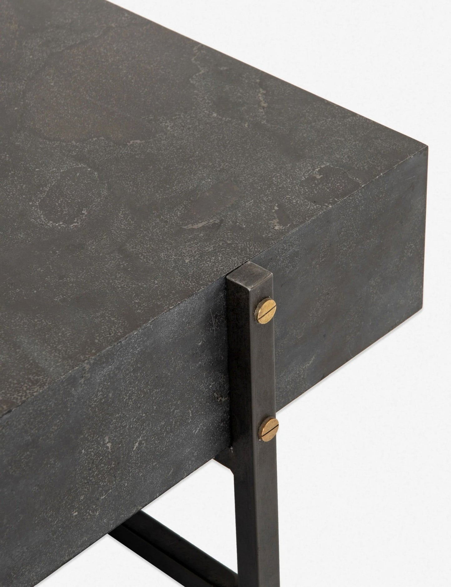 Close-up of the Keppler Square Coffee Table’s corner, showing its dark textured metal surface and legs joined by gold-tone screws. The clean lines highlight its industrial design.
