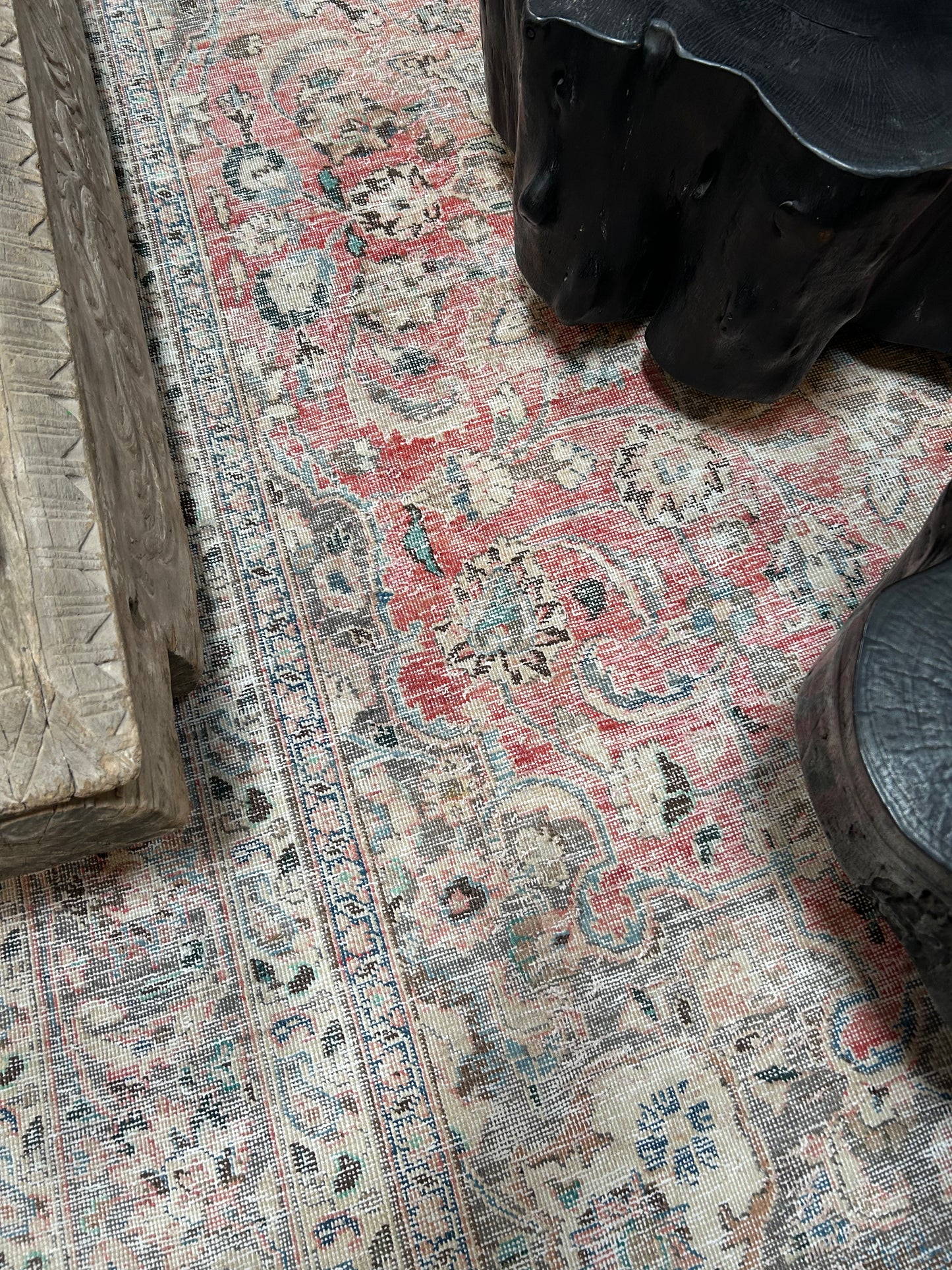 A Vintage Area Rug in ivory, grey, and pink with intricate floral and geometric patterns lies partially beneath dark sculpted office furniture and a carved light wood bench.