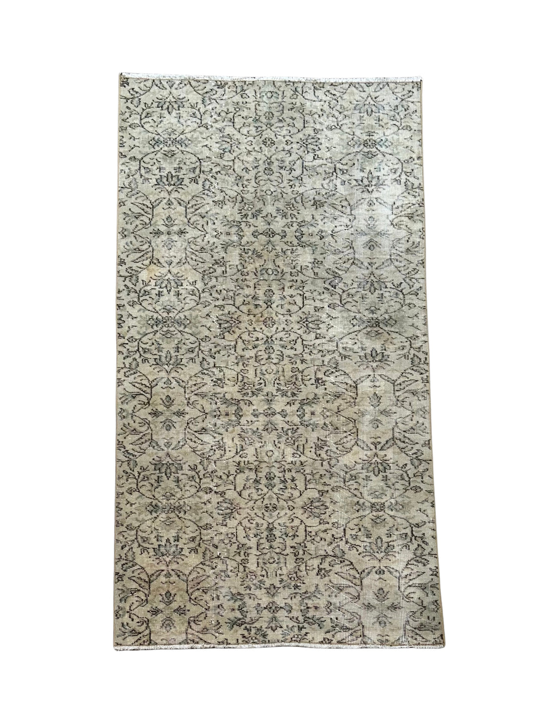 The Vintage Turkish Rug 4x7 features a light beige background with intricate, repeating floral and vine designs in dark gray tones, offering a slightly faded, vintage look. Shown photographed on a white background.