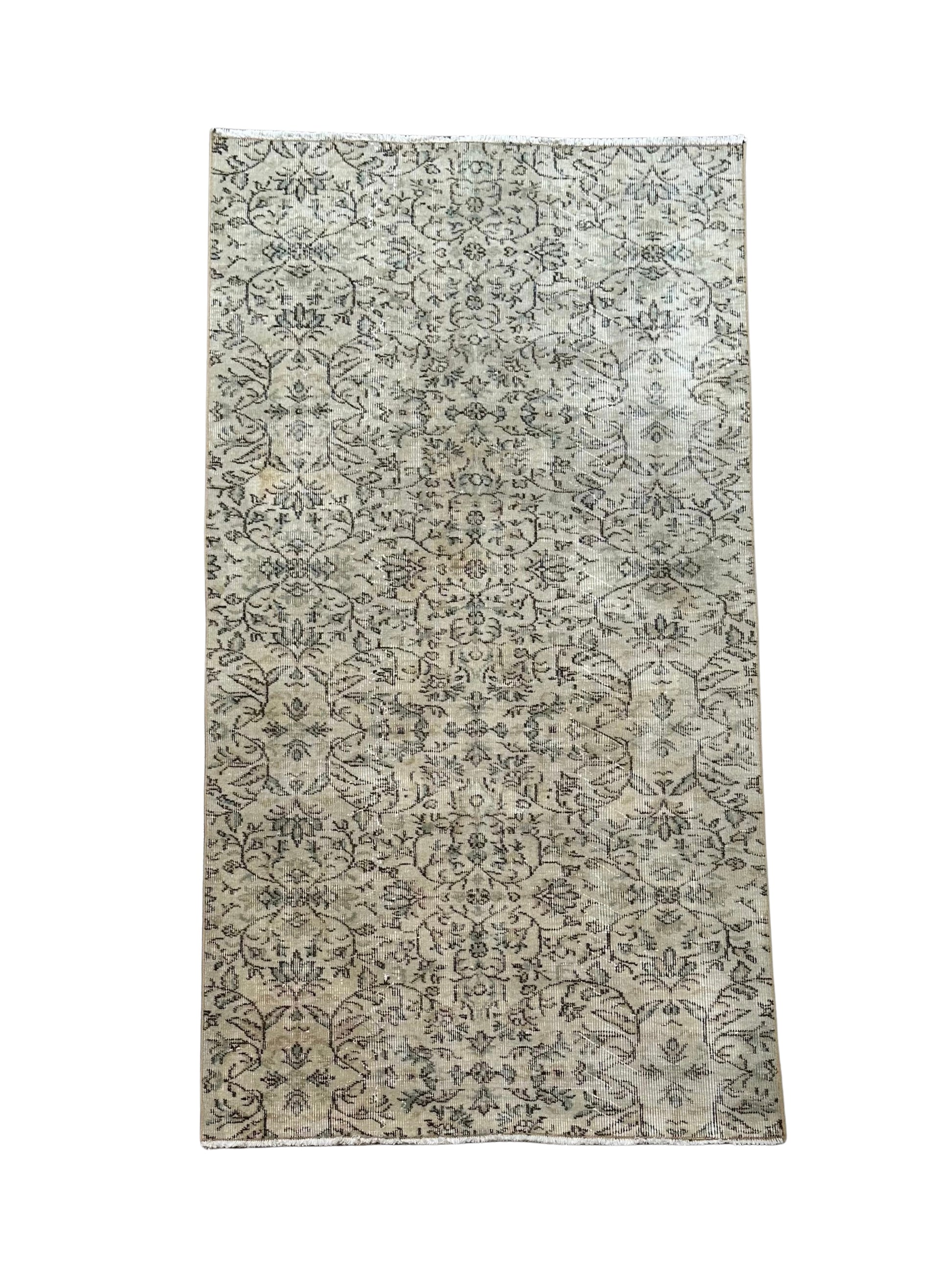 The Vintage Turkish Rug 4x7 features a light beige background with intricate, repeating floral and vine designs in dark gray tones, offering a slightly faded, vintage look. Shown photographed on a white background.