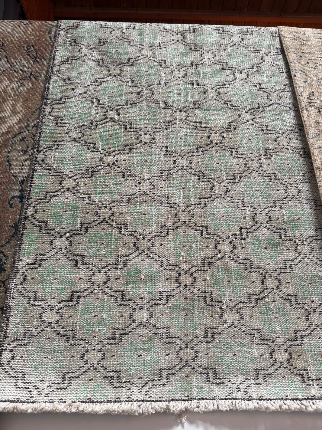 The Vintage Turkish Runner Rug is a rectangular 2'5" x 6' sage runner with a faded geometric pattern in green, gray, and black tones. It has a slightly worn look and fringed edges on the near side.