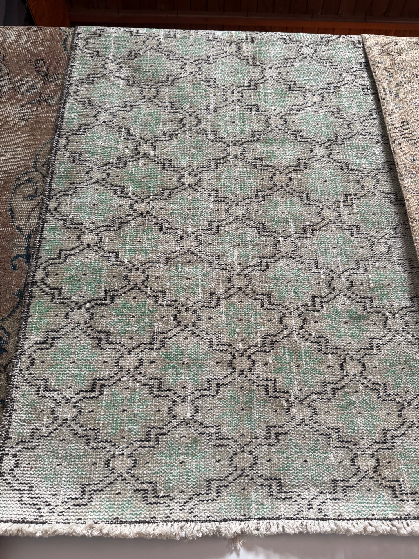 The Vintage Turkish Runner Rug is a rectangular 2'5" x 6' sage runner with a faded geometric pattern in green, gray, and black tones. It has a slightly worn look and fringed edges on the near side.