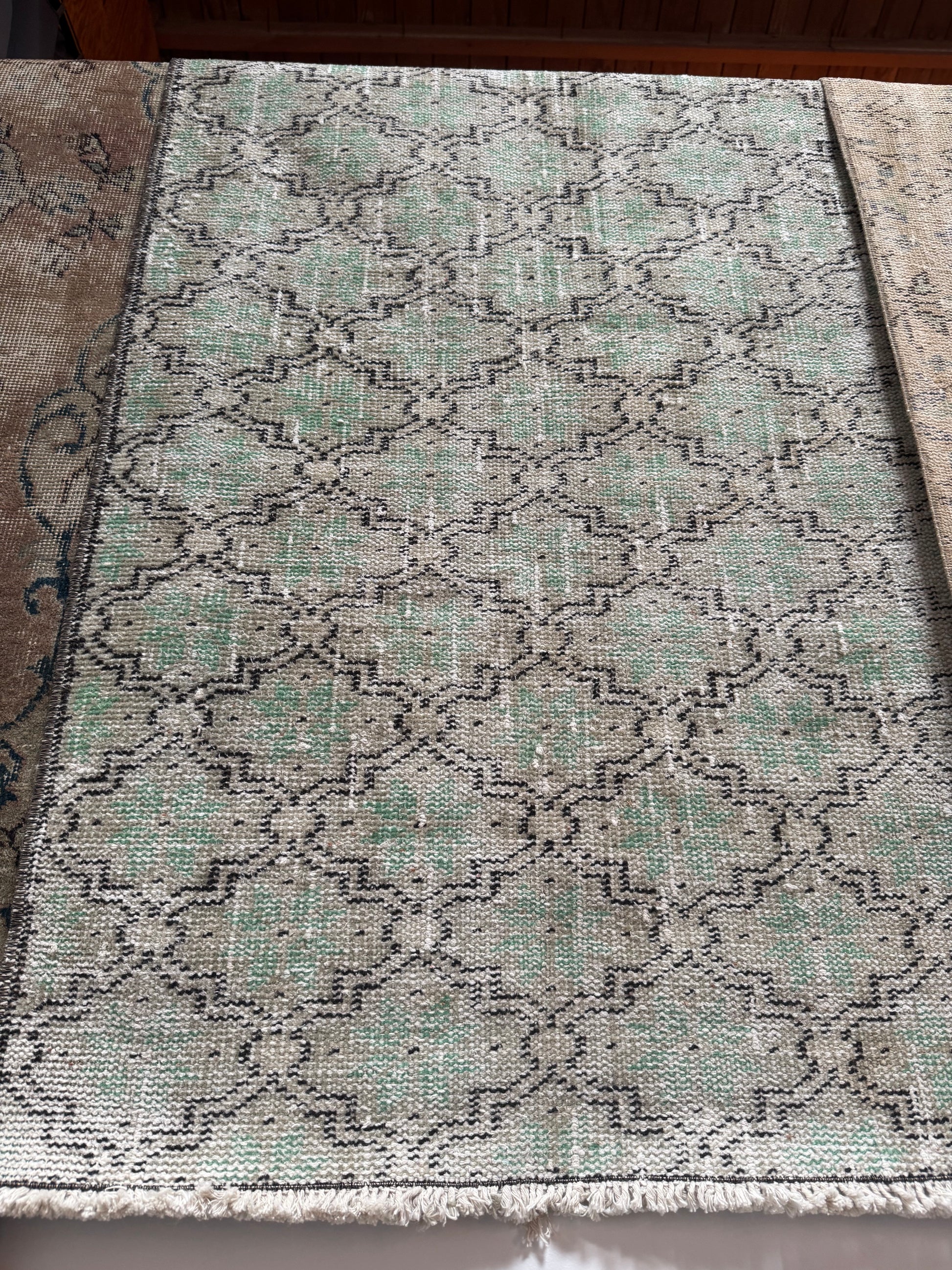 The Vintage Turkish Runner Rug is a rectangular 2'5" x 6' sage runner with a faded geometric pattern in green, gray, and black tones. It has a slightly worn look and fringed edges on the near side.