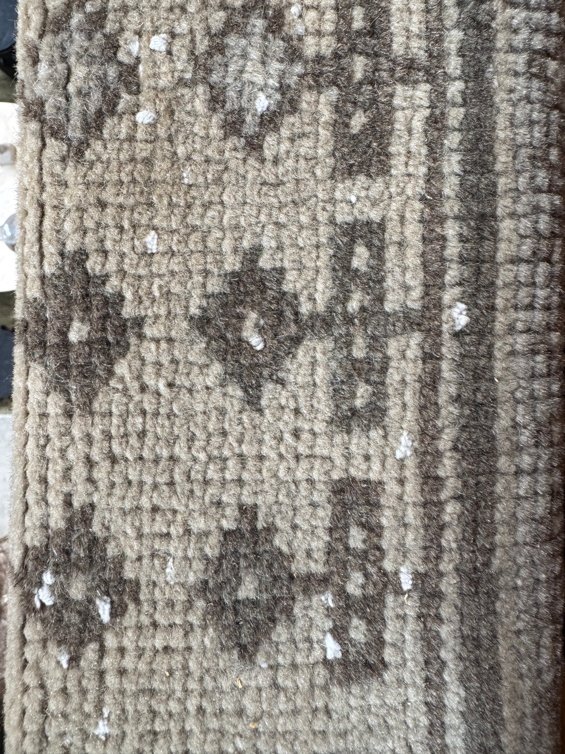 A close-up of the Vintage Turkish Runner Rug in beige and brown geometric patterns, with small white debris scattered across its surface.