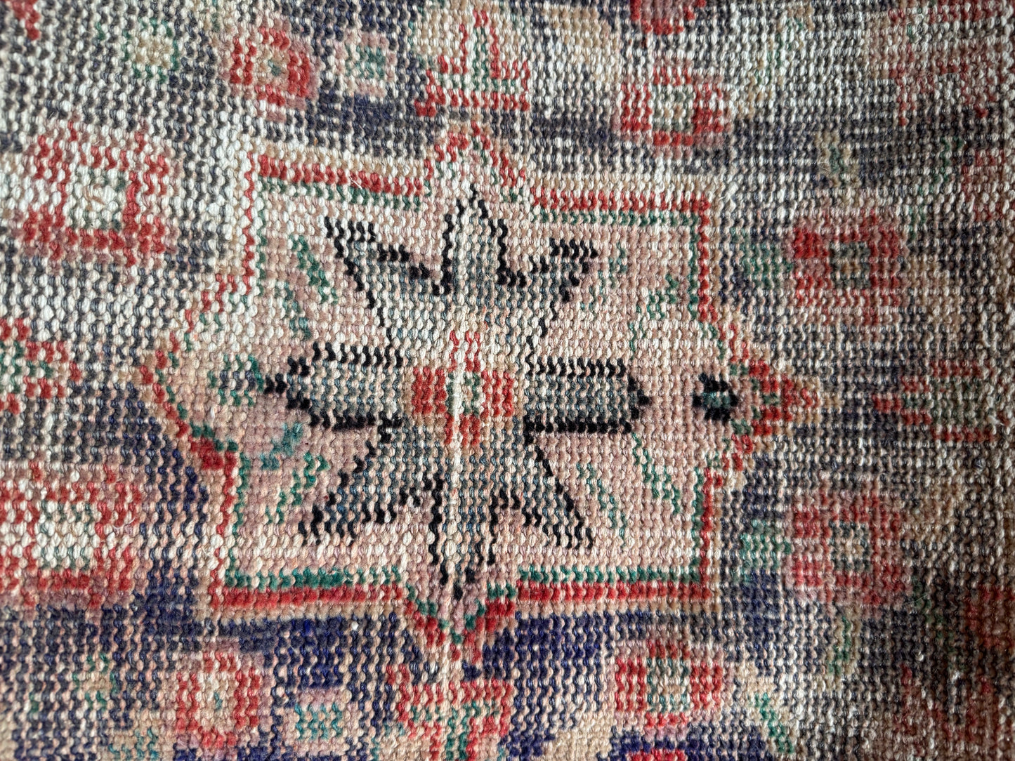 A close-up of the Vintage Turkish Runner Rug reveals a central eight-pointed star in black and white, framed by red, blue, and beige geometric shapes. The rug’s woven texture and gently faded colors add to its unique charm.