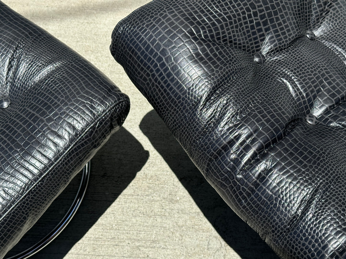 Close-up of two black croc leather cushions with lizard-skin texture from the Vintage Chrome and Leather Recliner & Ottoman, resting on smooth concrete in bright sunlight.