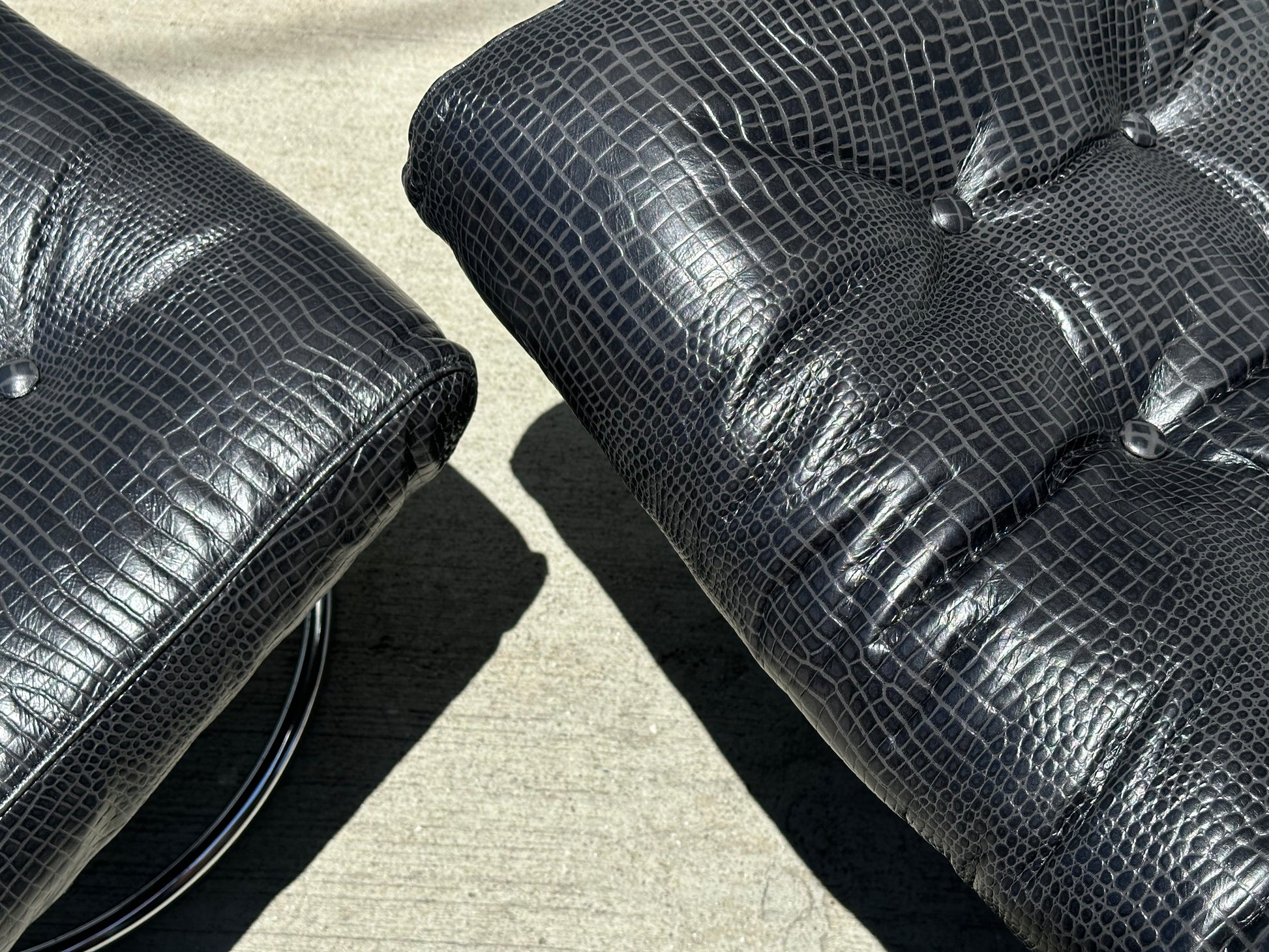 Close-up of two black croc leather cushions with lizard-skin texture from the Vintage Chrome and Leather Recliner & Ottoman, resting on smooth concrete in bright sunlight.