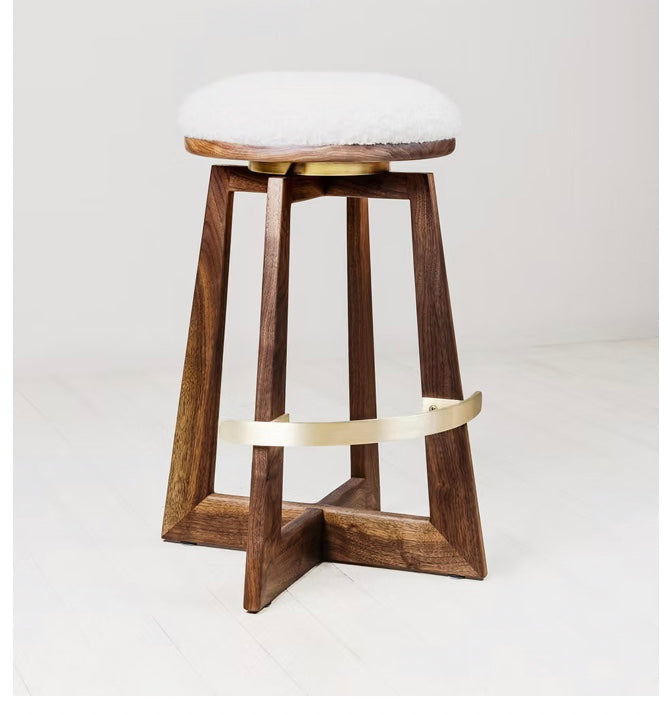 The Walnut and Brass Swivel Bar Stool features a wooden base with angled legs, a gold-colored metal footrest, and a round cushioned white seat, all set against a light background.