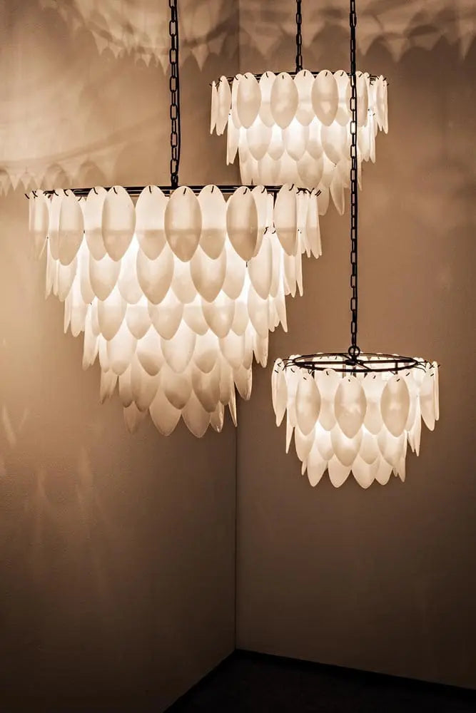 Three Opaque Glass Petal Chandeliers hang from the ceiling, each featuring layered glass petals for a contemporary look and casting soft, decorative shadows on the walls.