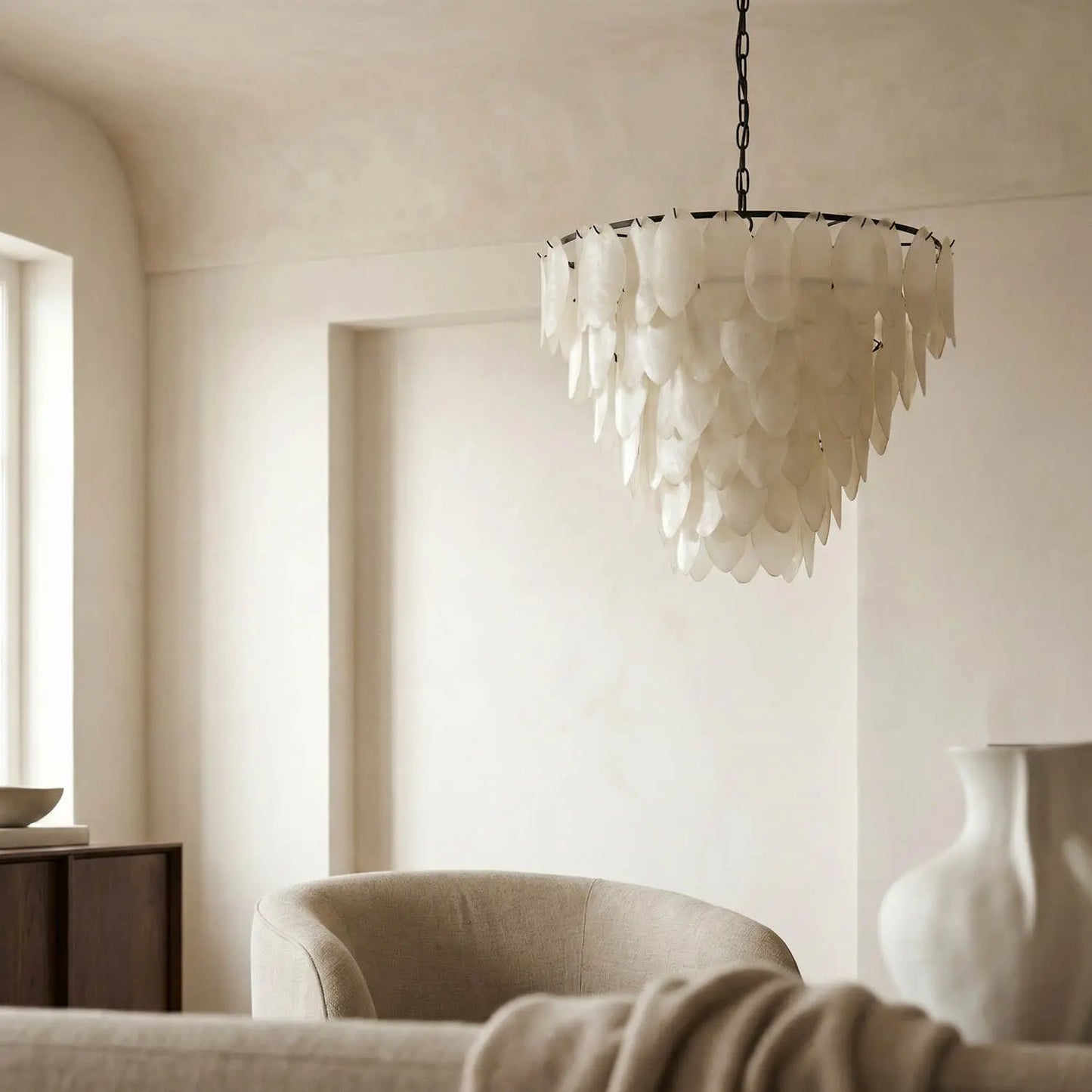 Elegant, neutral-toned living room with soft beige furniture, a sculptural vase, and the Opaque Glass Petal Chandelier hanging from the ceiling as sunlight pours in through a large window.
