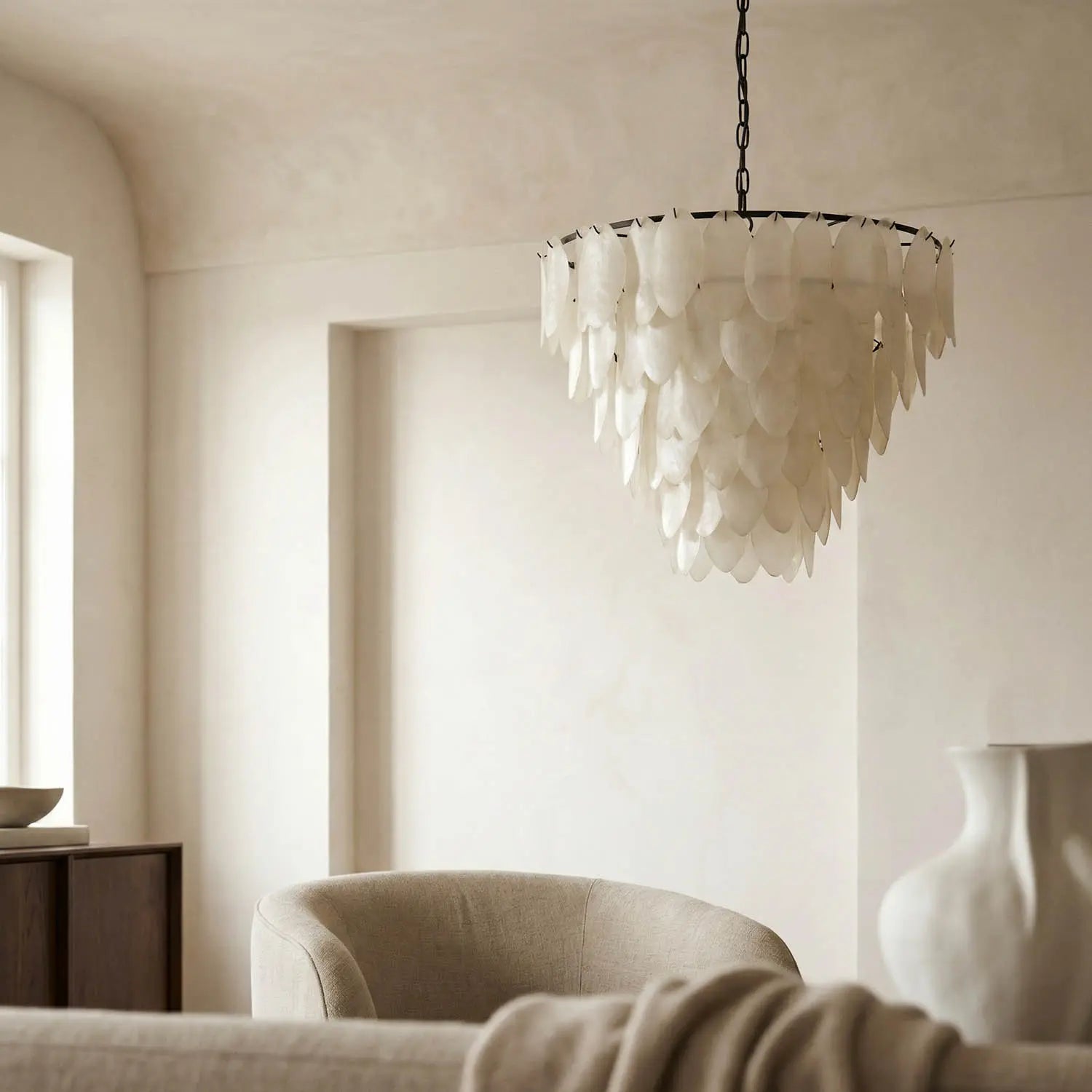 Elegant, neutral-toned living room with soft beige furniture, a sculptural vase, and the Opaque Glass Petal Chandelier hanging from the ceiling as sunlight pours in through a large window.