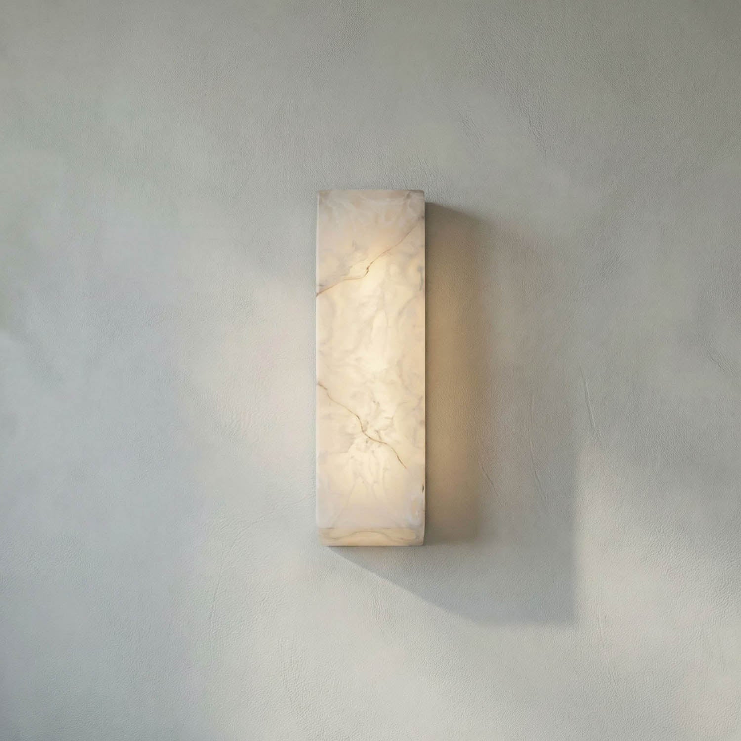 The Rectangular Sconce, crafted from marbled translucent material, emits a soft warm glow, making it ideal for contemporary lighting on a smooth light gray wall.