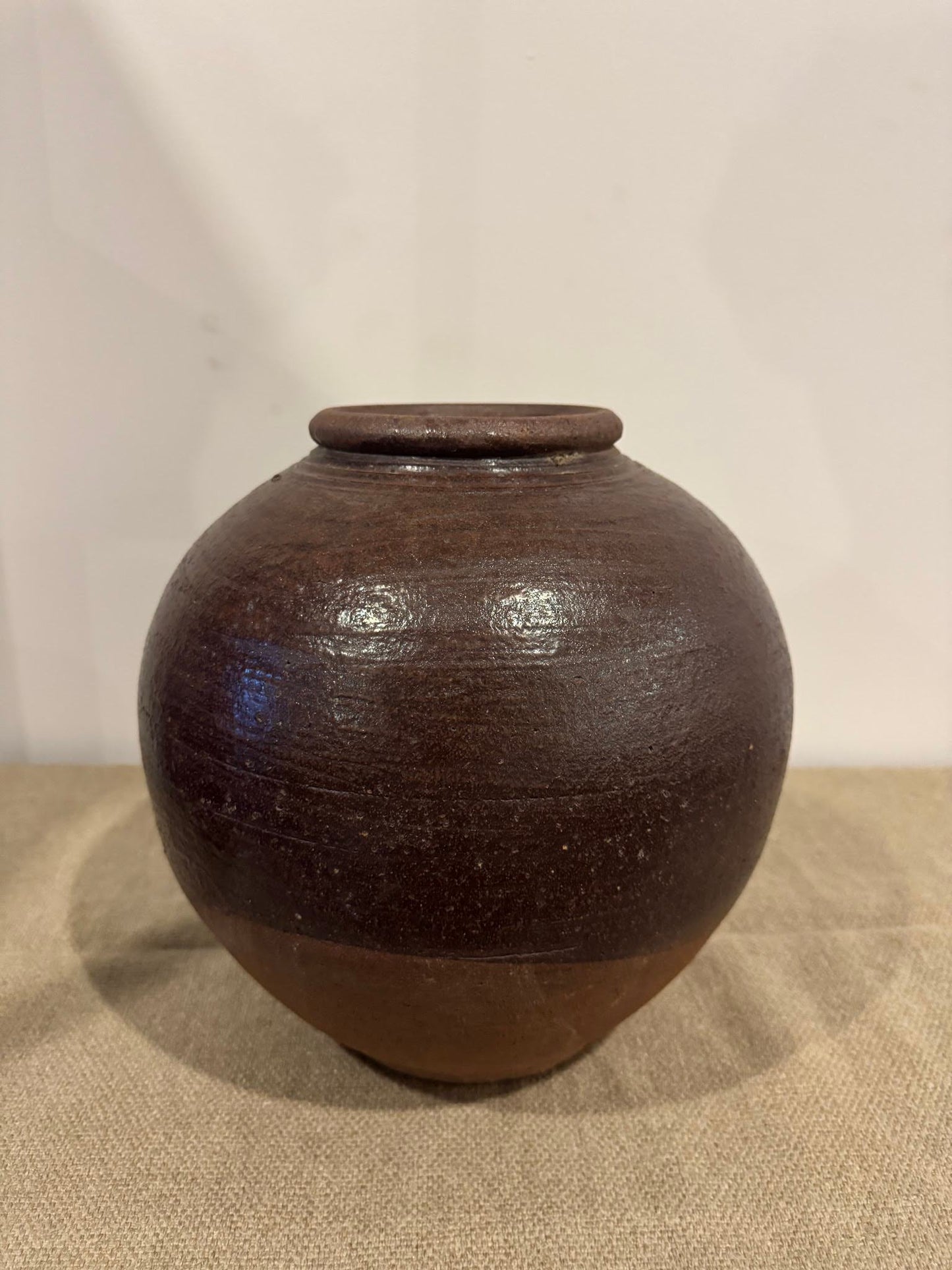 The Large Brown Pot, measuring 12 inches in height and 11 inches in width, features a small flat lid and rests on a beige fabric surface against a plain light background.