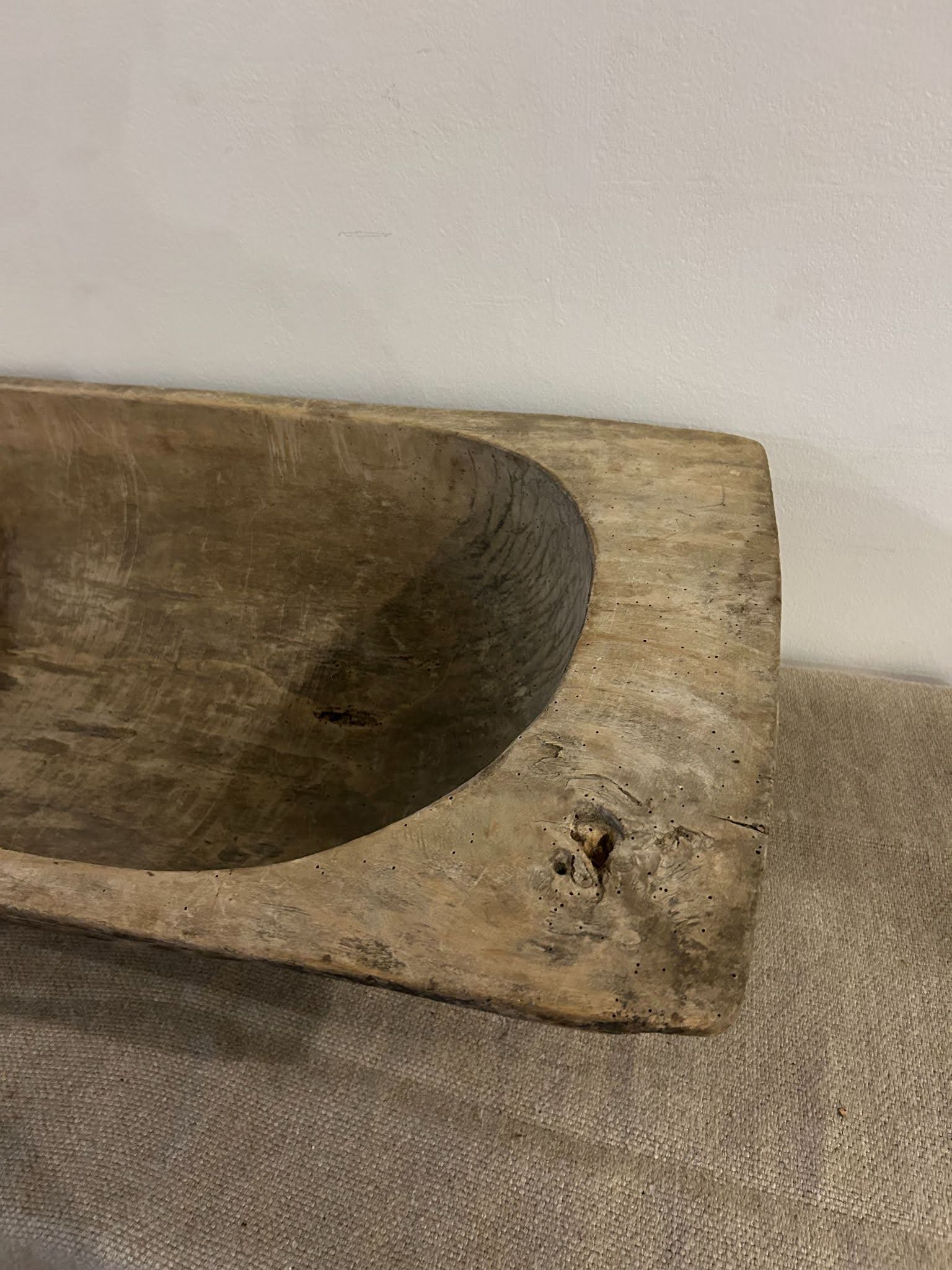 A close-up of the Large Light Display Bowl—a rustic, rectangular wooden piece with visible grain—evoking the sleek lines of a 33.5-inch bathtub, displayed on textured beige fabric before a plain white wall.