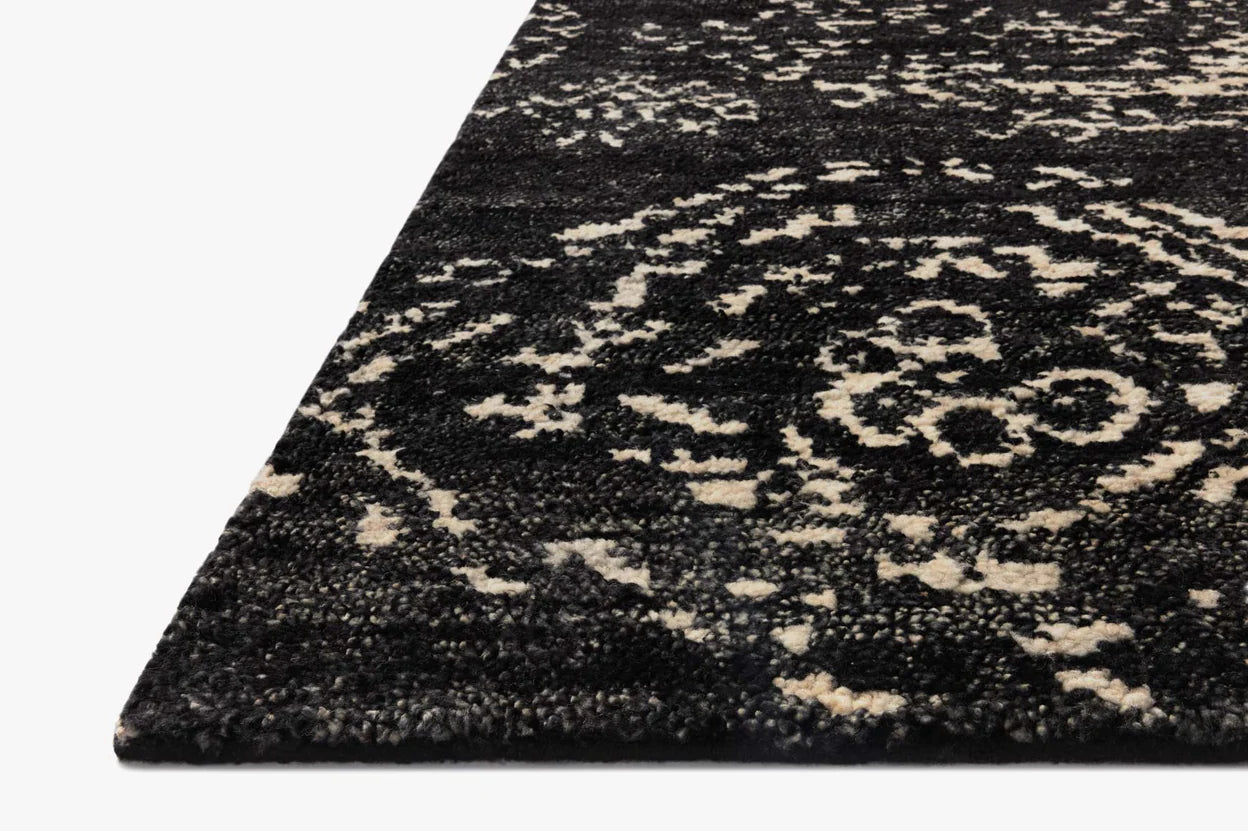 Close-up view of the corner of the Abstract Diamond Wool Rug 8 x 10, featuring a hand knotted black base with an intricate, distressed white and gray floral pattern on a white background.
