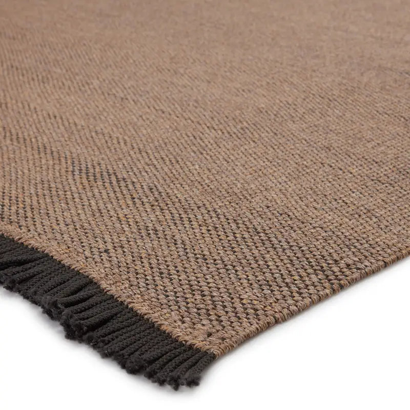 Close-up of the Handcrafted Taupe Rug, size 5'x8', featuring a woven textured pattern and short black fringe on the edge, displayed on a white background.