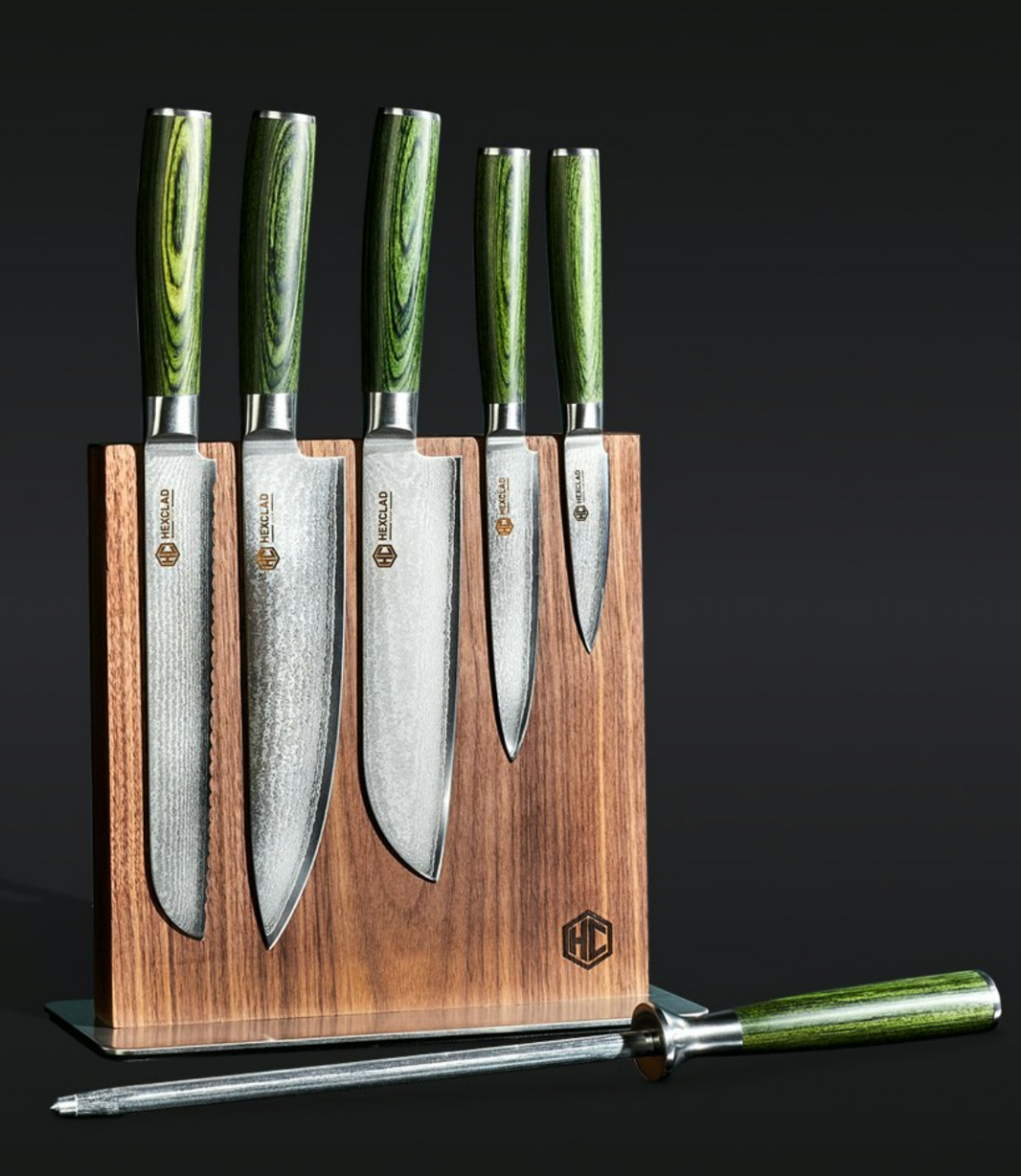 The Hexclad Steel Knife Block features five kitchen knives with green handles and a matching honing steel, all neatly stored in a wooden block and displayed on a black background.