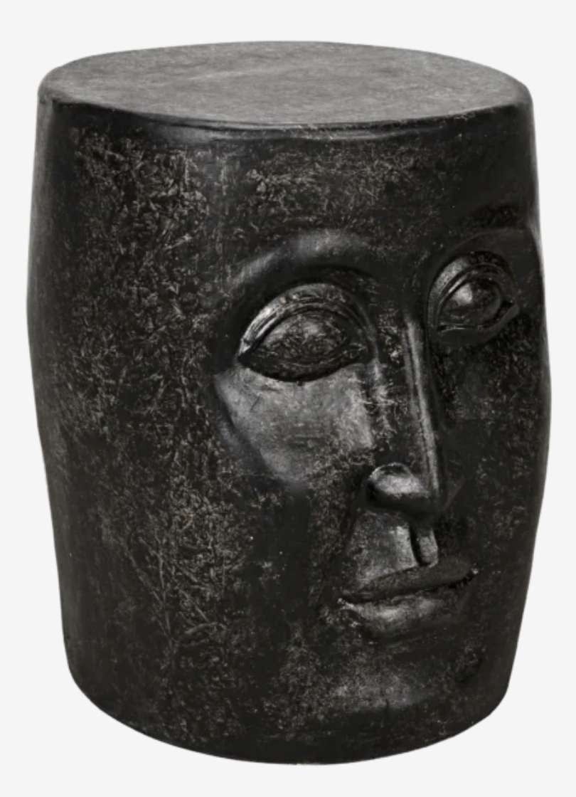 The Single-Face Stool is a black sculptural accent table featuring detailed eyes, nose, and lips carved onto its front, resembling a human face.