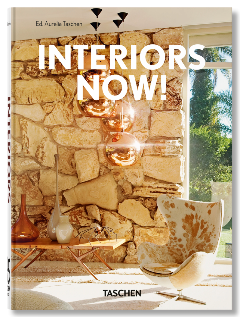 Book cover of *Interiors Now! (45th Anniversary Edition)* features a chic living room with a stone accent wall, copper lighting, a white cowhide chair, and large windows—ideal inspiration for contemporary interior design lovers.