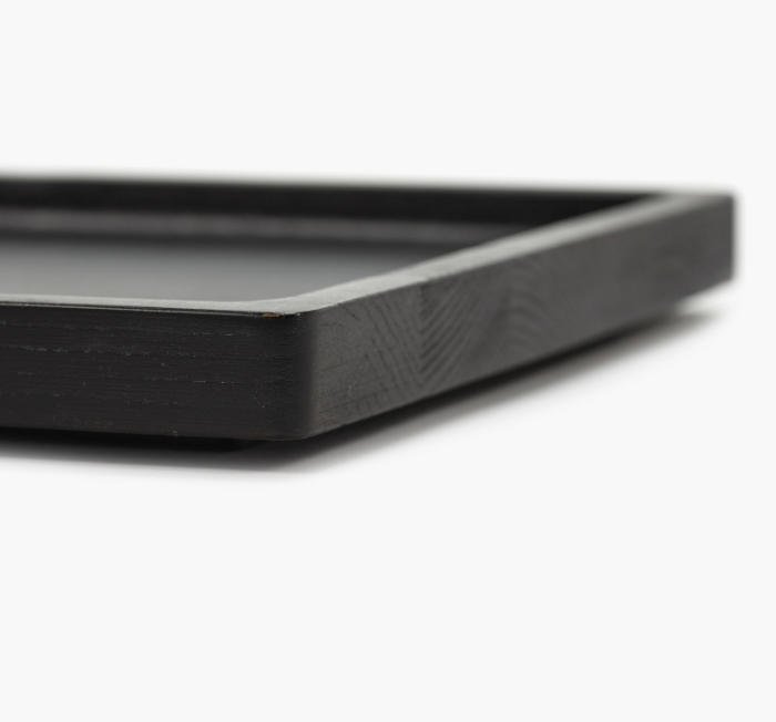 Close-up view of the corner of the Large Black Arch Tray, a rectangular serving tray with smooth edges and a carbonised ash finish, resting on a white surface.