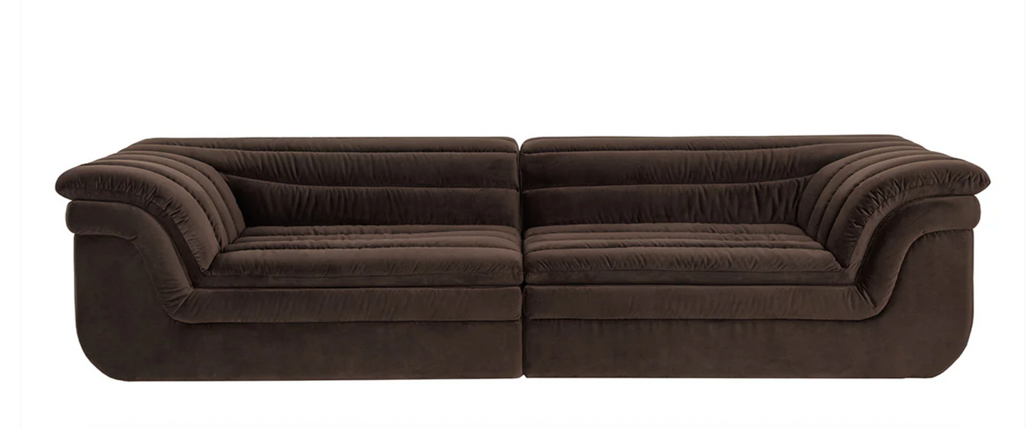 The Low-slung sculptural sofa features modern channel tufting, low-profile design, and deep plush details in dark brown fabric, elegantly displayed against a plain white background.