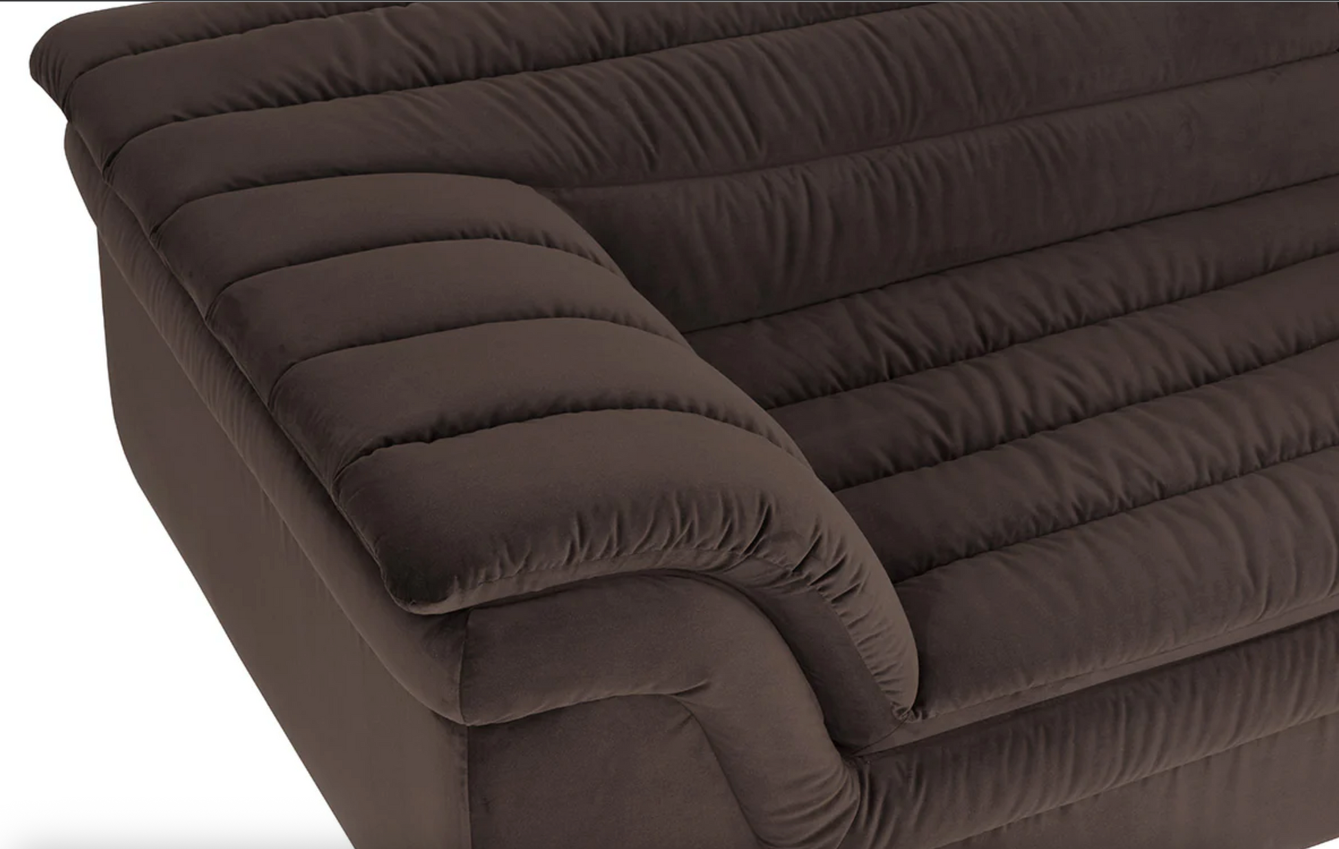 A close-up of the Low-slung sculptural sofa highlights its dark brown, channel tufted design with plush, velvety upholstery and rounded, padded edges on the seat, backrest, and armrest.