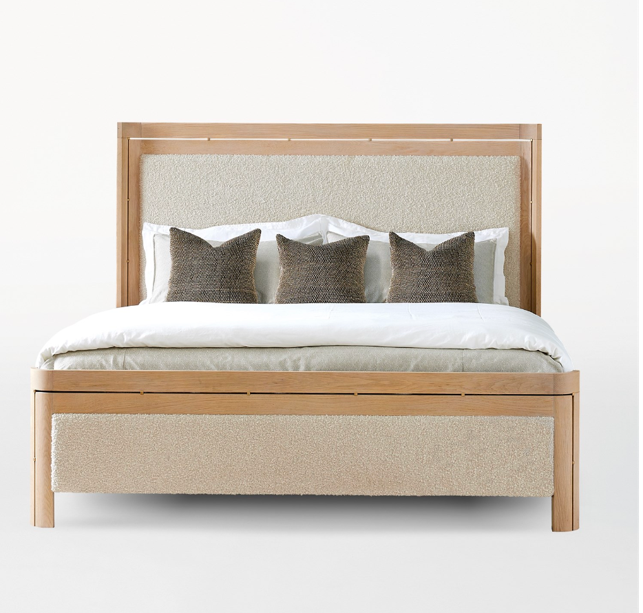 The Light Oak Upholstered Queen Bed Frame features a modern wooden design with a light upholstered headboard and footboard, dressed in white bedding, four dark textured throw pillows, and two white pillows.