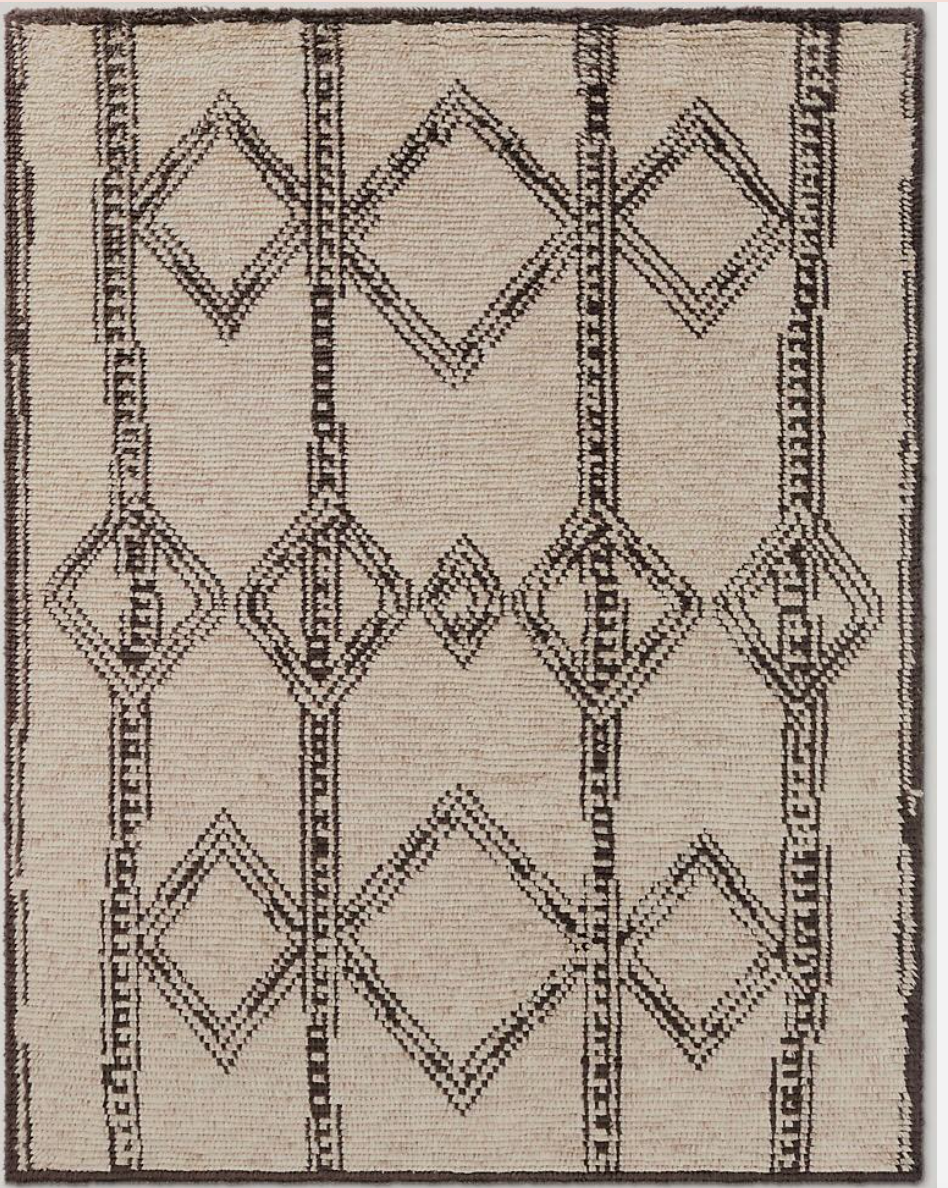The Handwoven Moroccan Wool Rug is a large beige area rug featuring black geometric lines with vertical stripes and diamond shapes for a modern, abstract look.