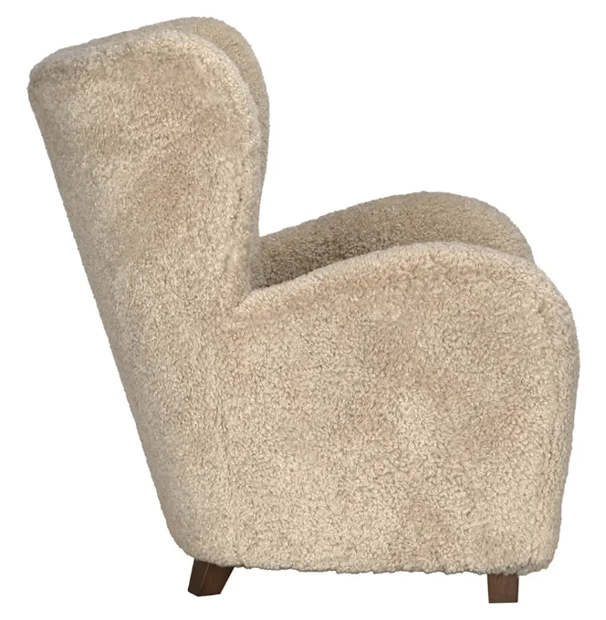 A side view of the Pola Chair shows its contemporary design, upholstered in beige, fluffy textured fabric with wooden legs and a curved backrest and armrests.