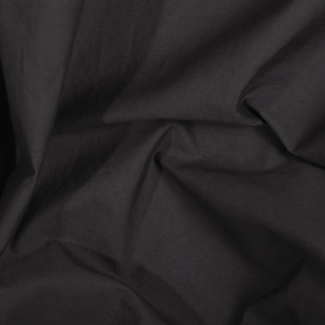 A close-up of the Riviera Cotton Hand Towel in Smoke reveals visible folds and creases, highlighting texture and shadows; its garment-dyed finish showcases a rich tone achieved with non-toxic dyes.