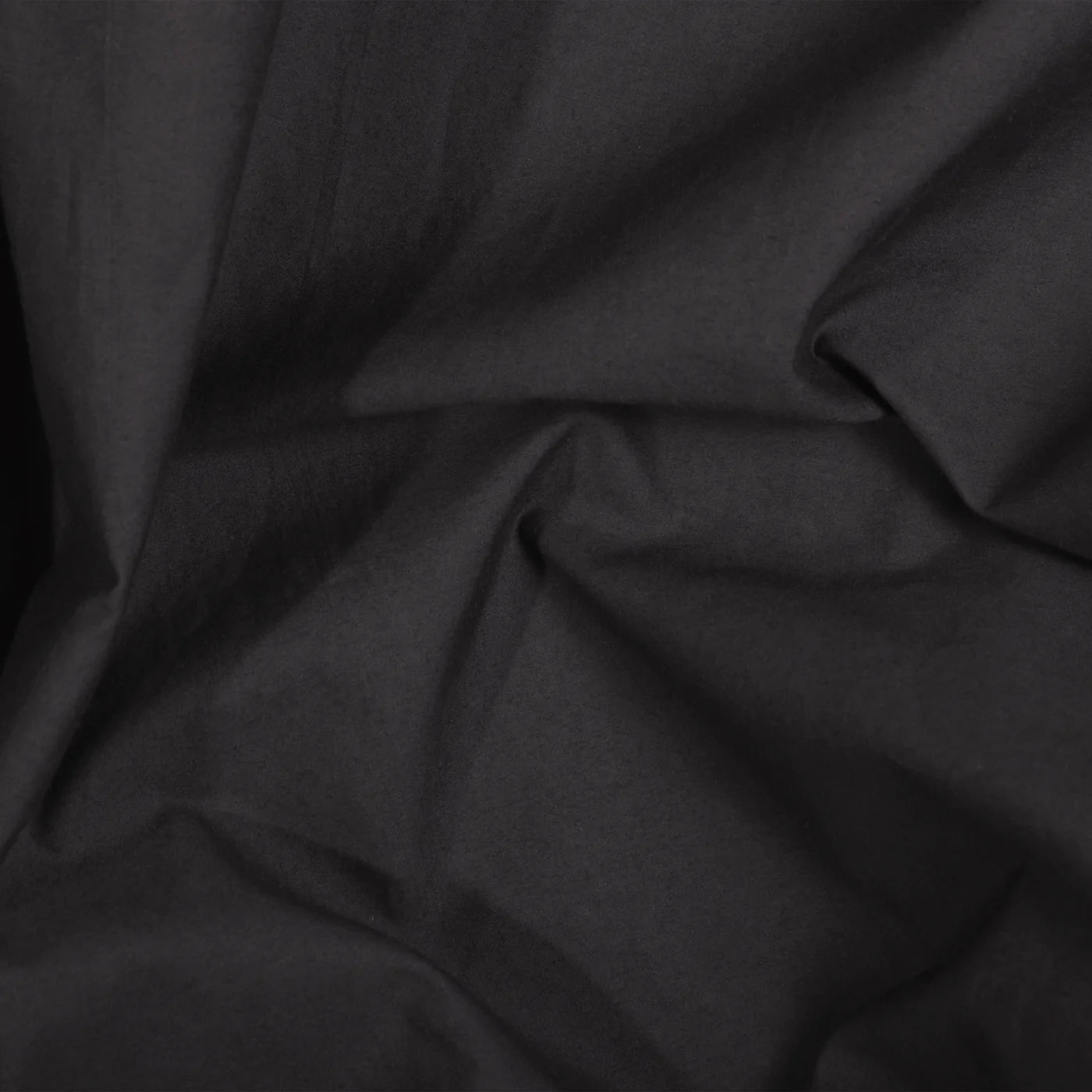 A close-up of the Riviera Cotton Hand Towel in Smoke reveals visible folds and creases, highlighting texture and shadows; its garment-dyed finish showcases a rich tone achieved with non-toxic dyes.