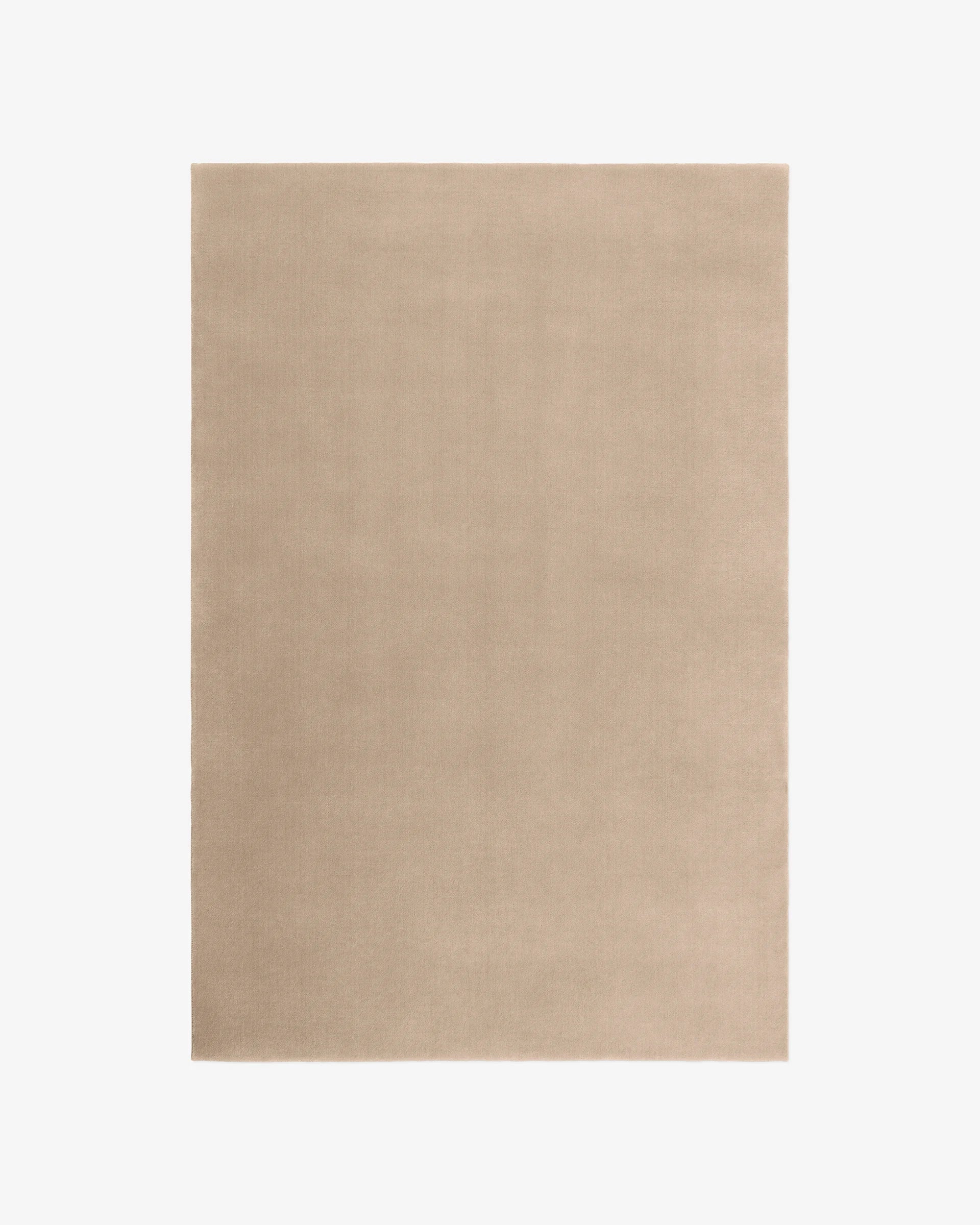 The Sand Wool Rug is a rectangular, solid beige rug with a smooth, even surface, displayed on a white background.